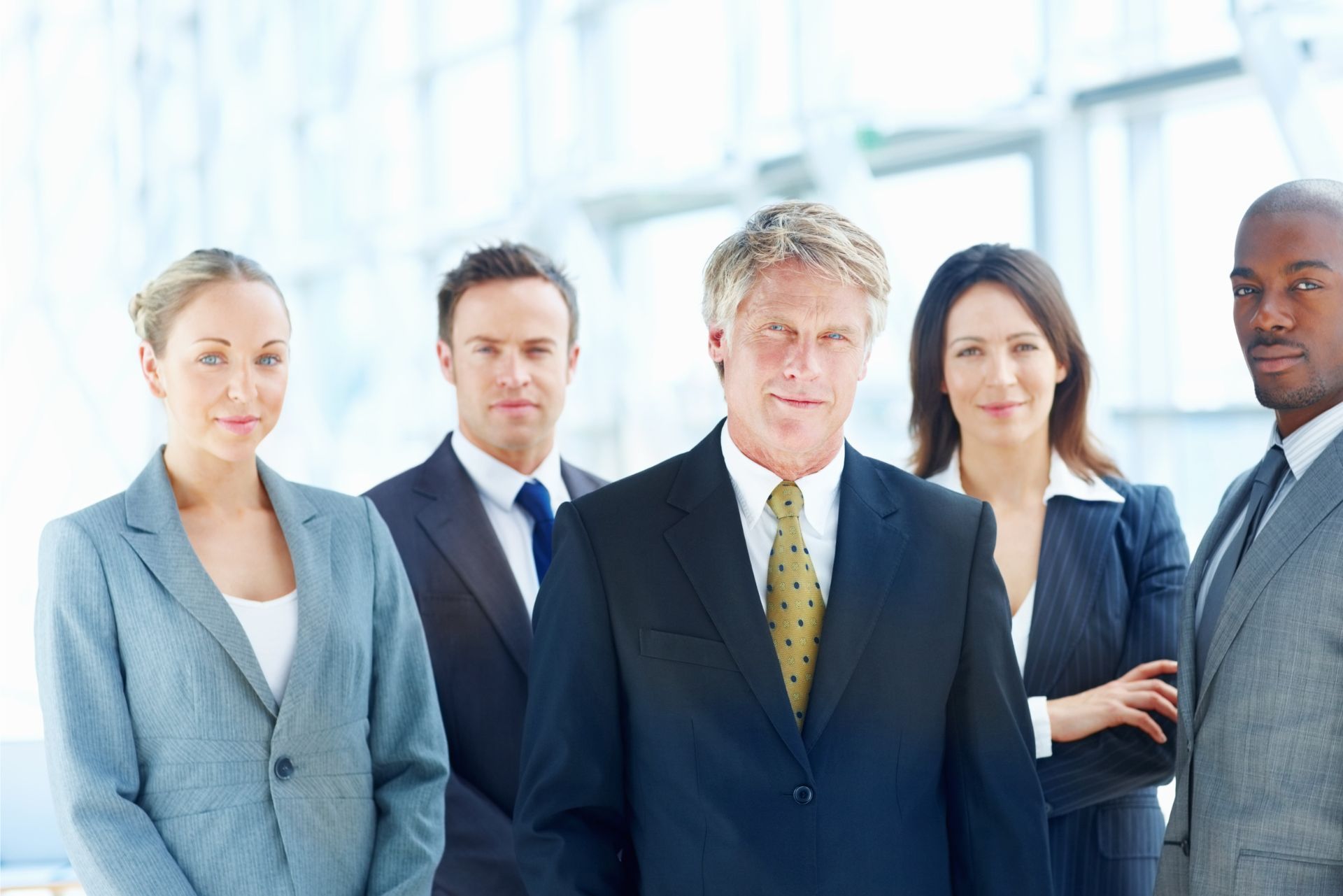 Five business professionals in suits standing together in a bright office setting