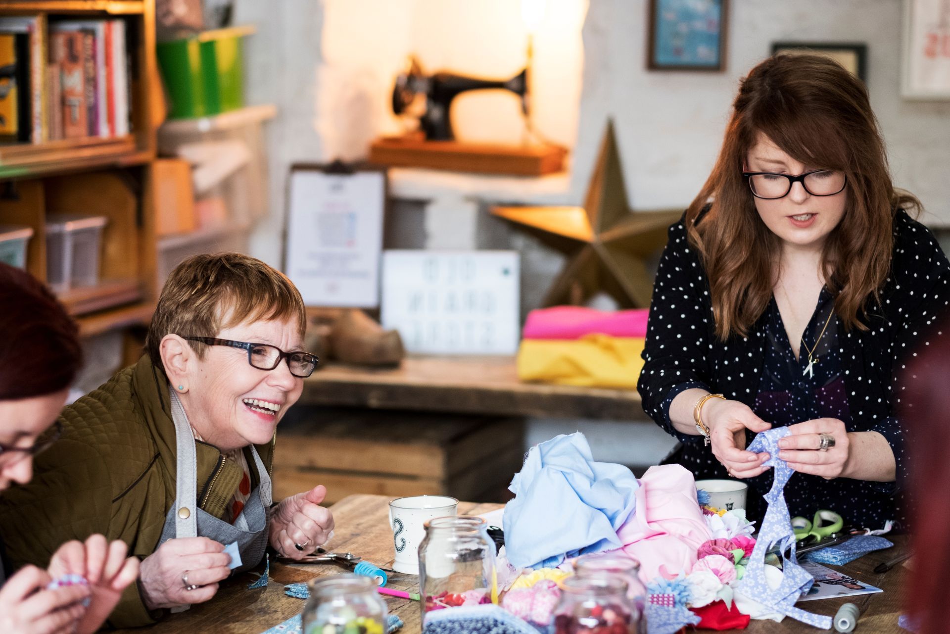 People crafting at a table with colorful supplies, smiling in a cozy workshop
