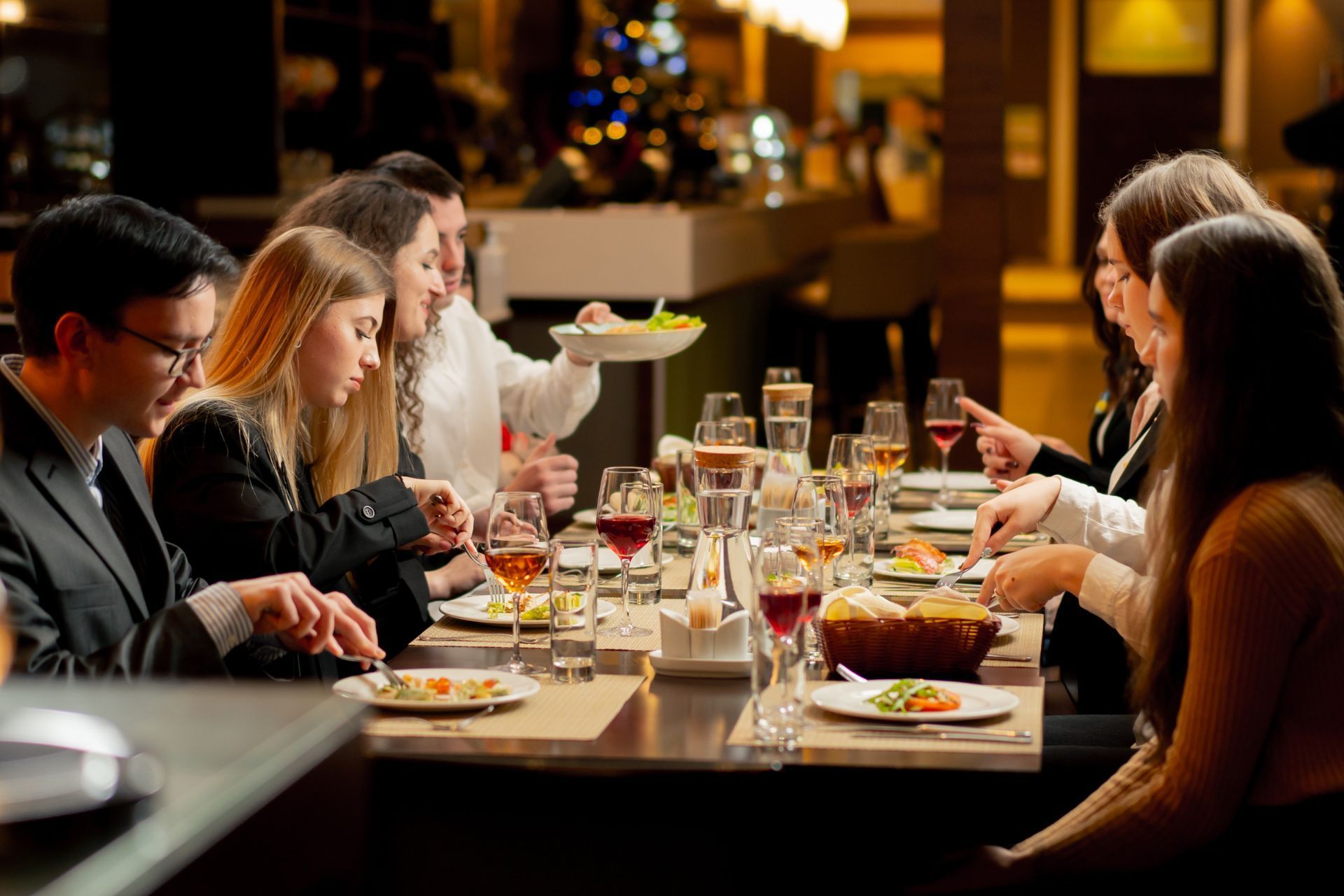 People dining and chatting around a restaurant table with wine glasses and plates in warm ambient light