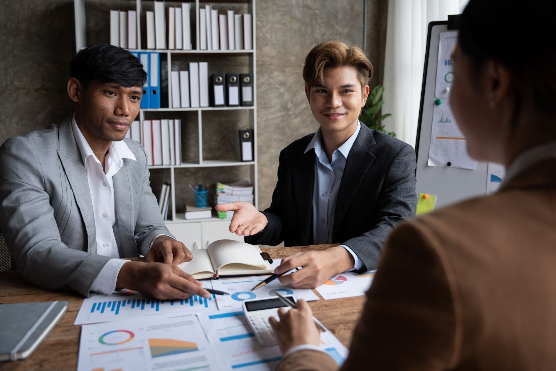 Business meeting with three people reviewing charts and documents at a desk in an office