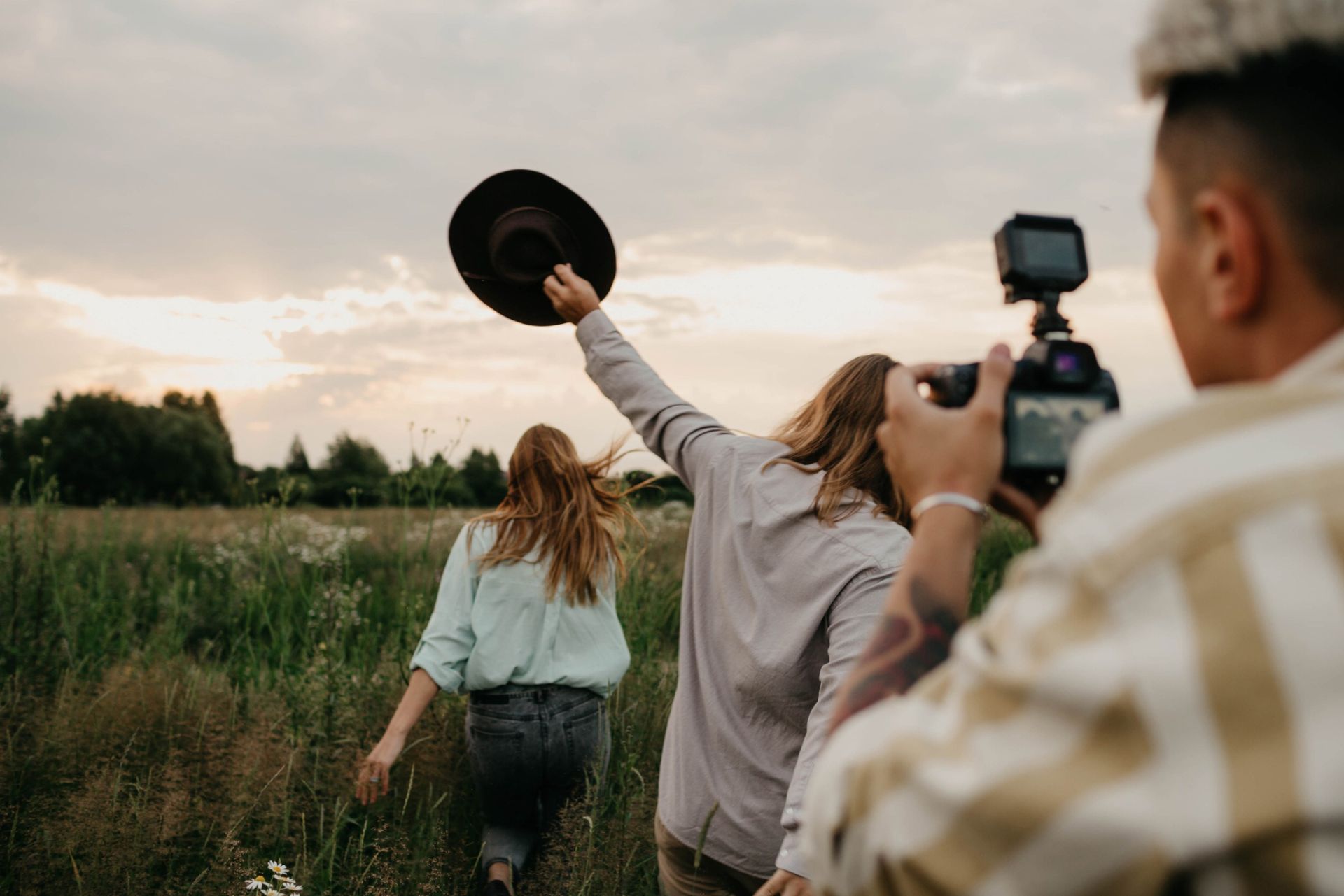 Friends walking through a field at sunset while filming a celebration outdoors