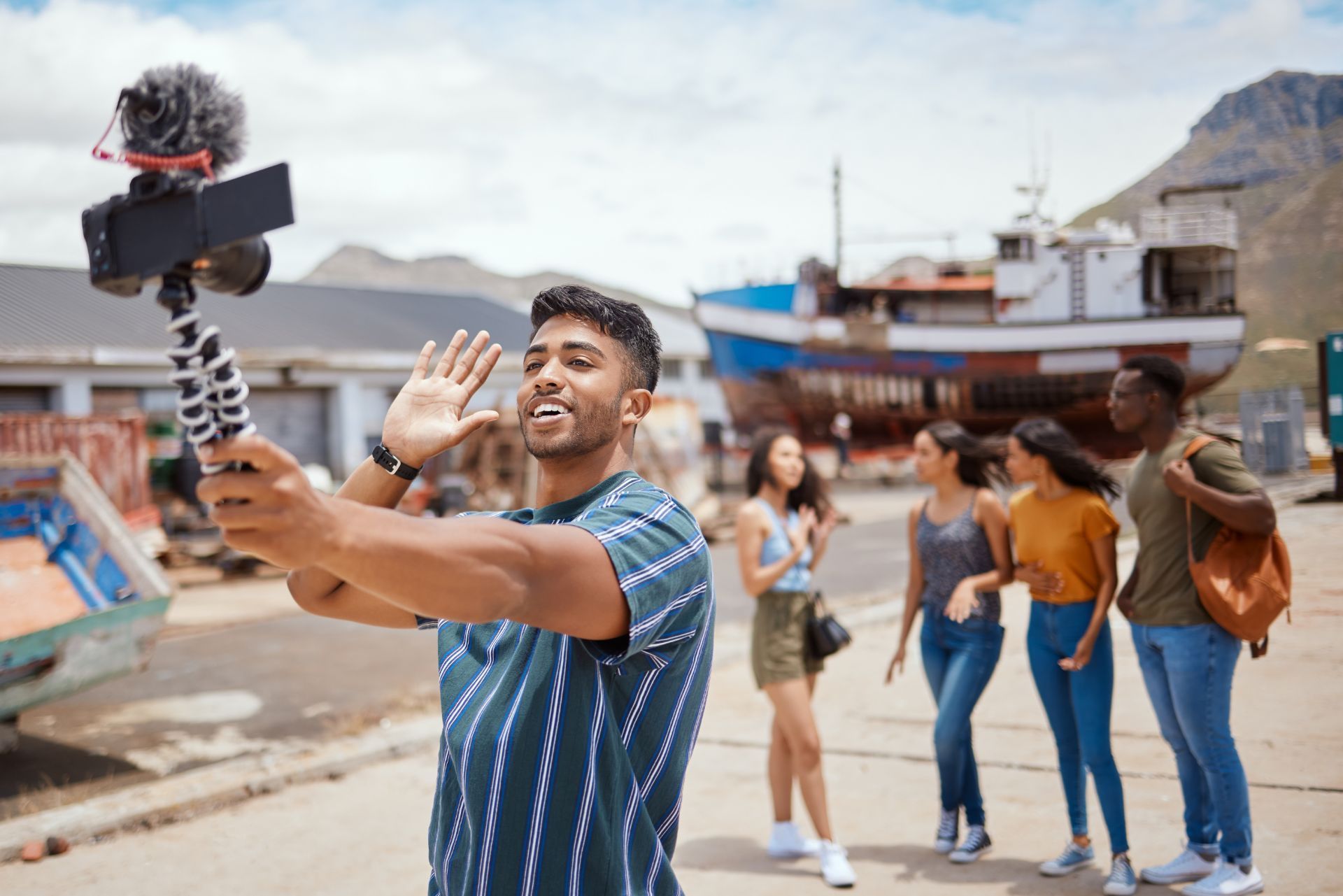 Man filming a selfie video outdoors with people walking behind him in a sunny street market