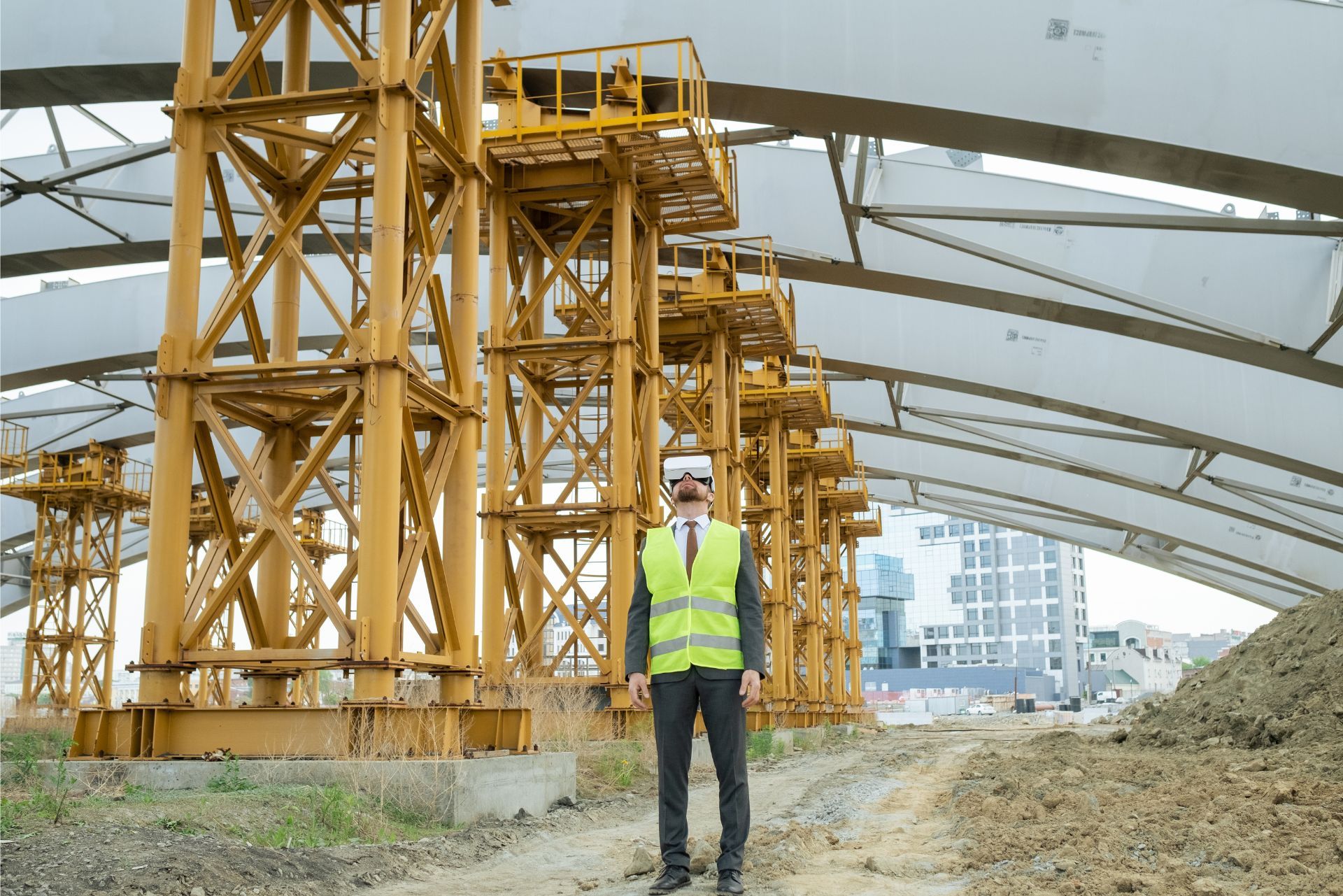 Construction worker in a yellow vest standing in a large industrial site with heavy steel framework.