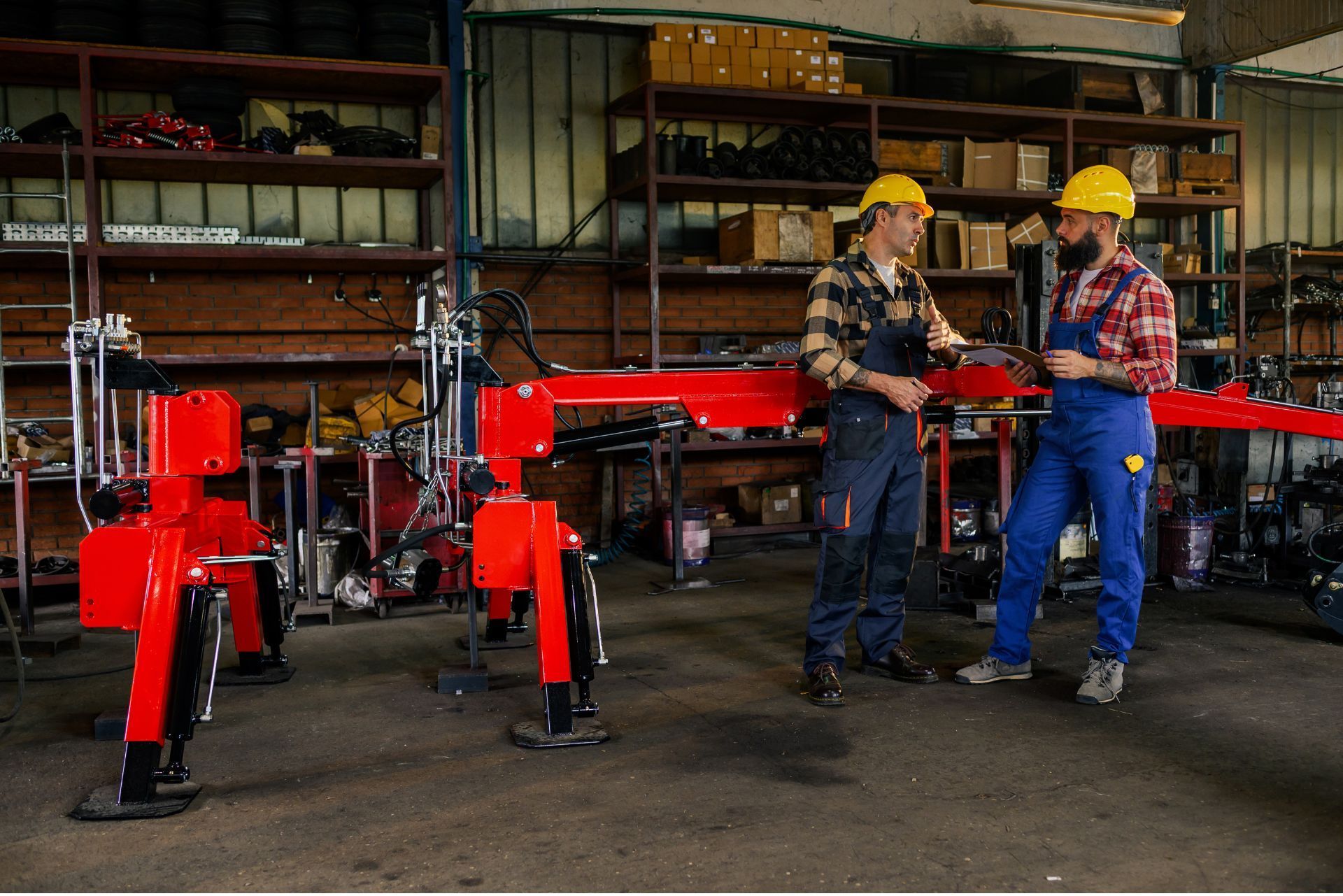 Two workers in hard hats beside red robotic equipment in an industrial workshop