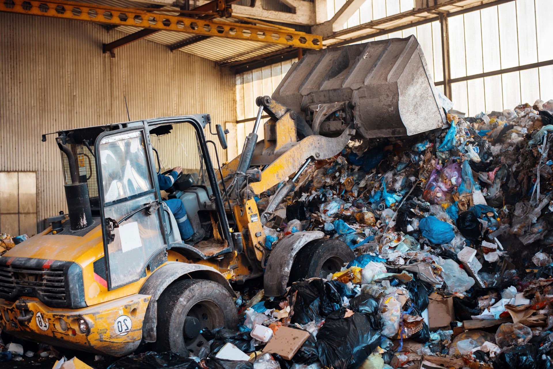 Front loader pushing a pile of mixed recyclables inside a warehouse, with a trash compactor nearby