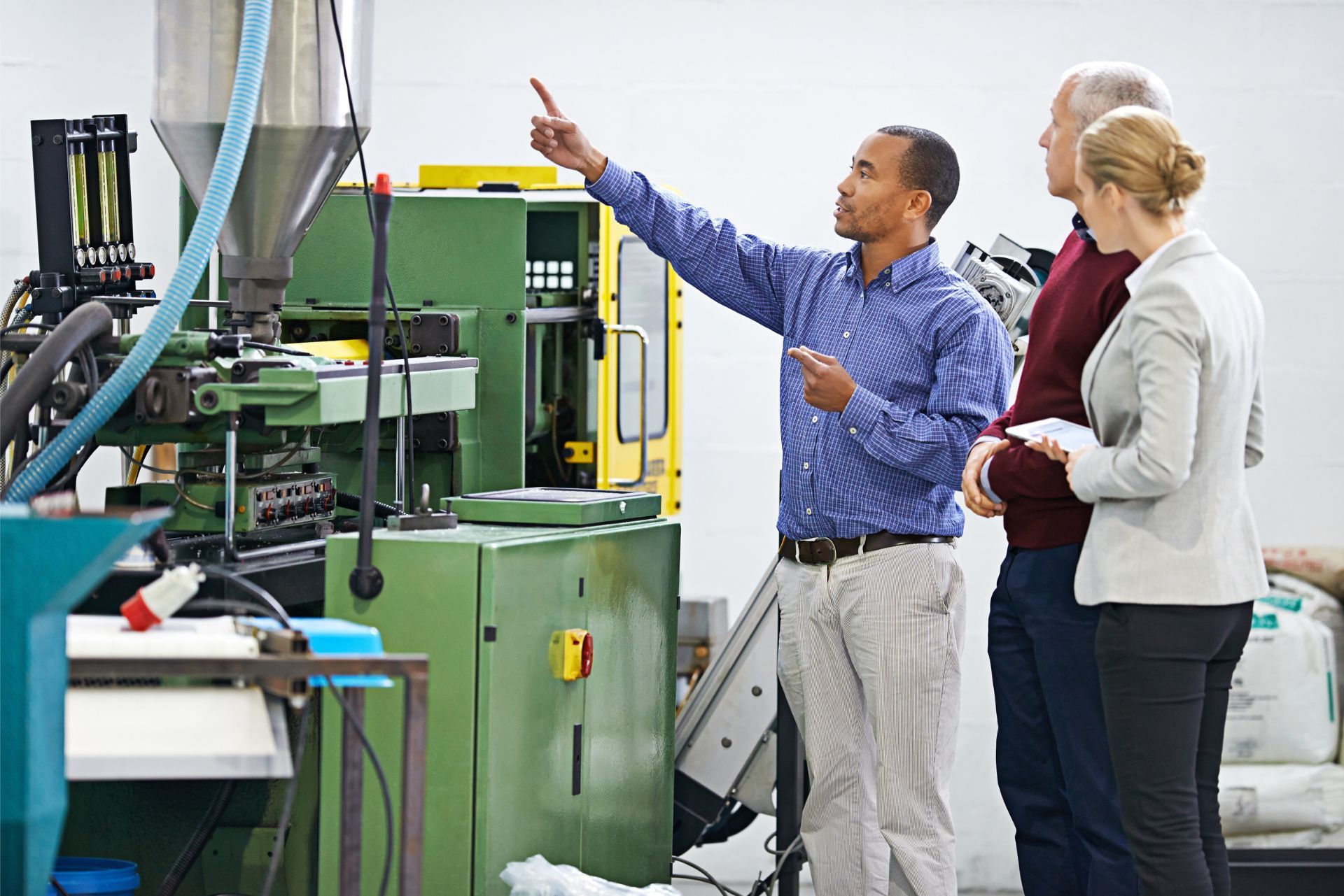Three people examining a green industrial machine in a factory, one pointing upward