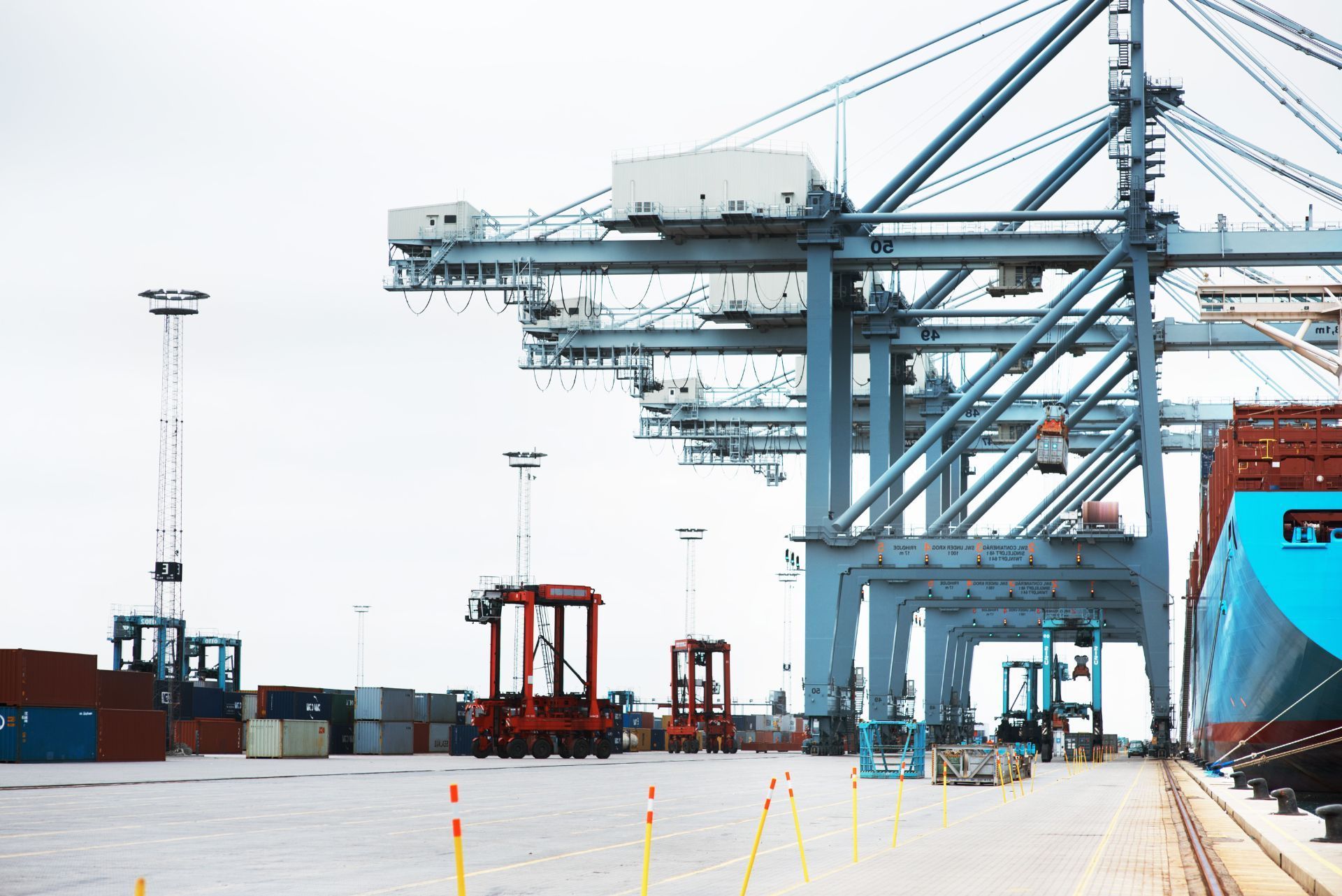 Port cranes loading cargo containers at a busy shipping port with a large ship docked nearby