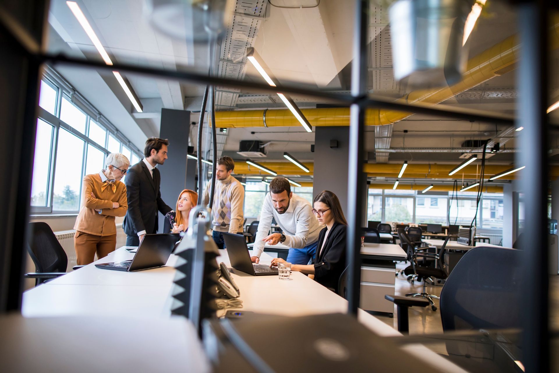 Colleagues meeting in a modern office, gathered around a conference table with computers and paperwork.
