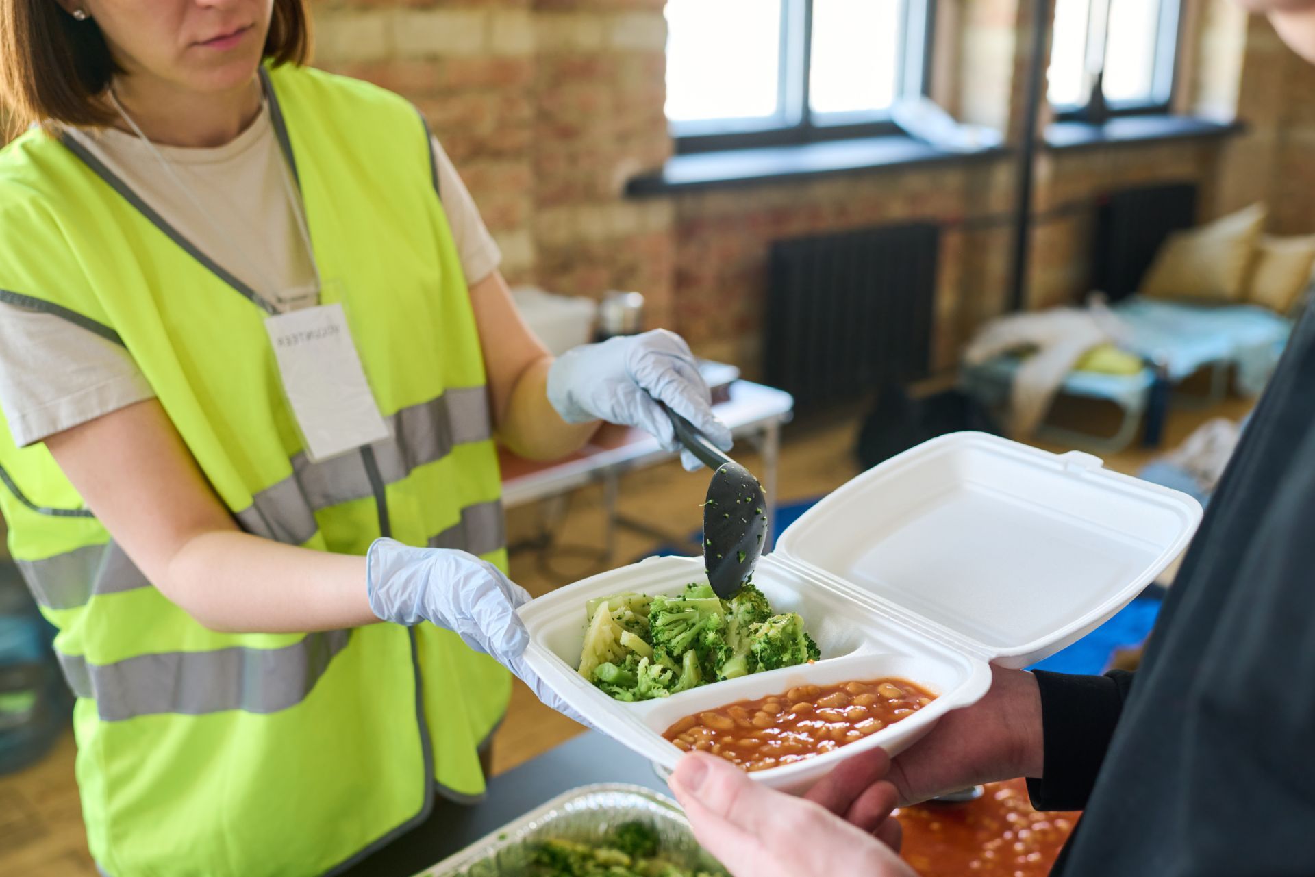 Volunteer serving food in a cafeteria, placing green vegetables into a takeout container