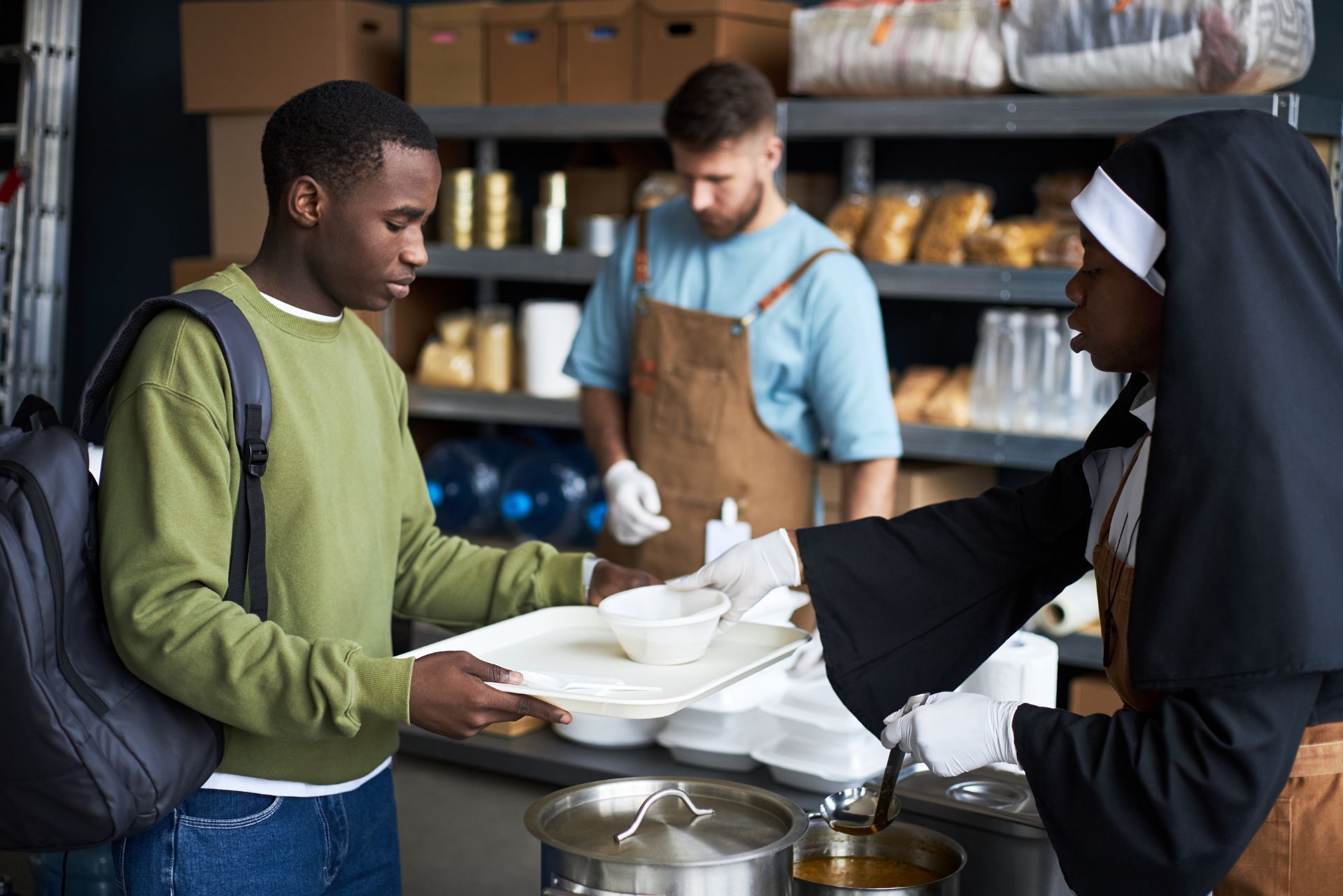 Volunteers serving meals at a community food pantry, with shelves of supplies in the background.