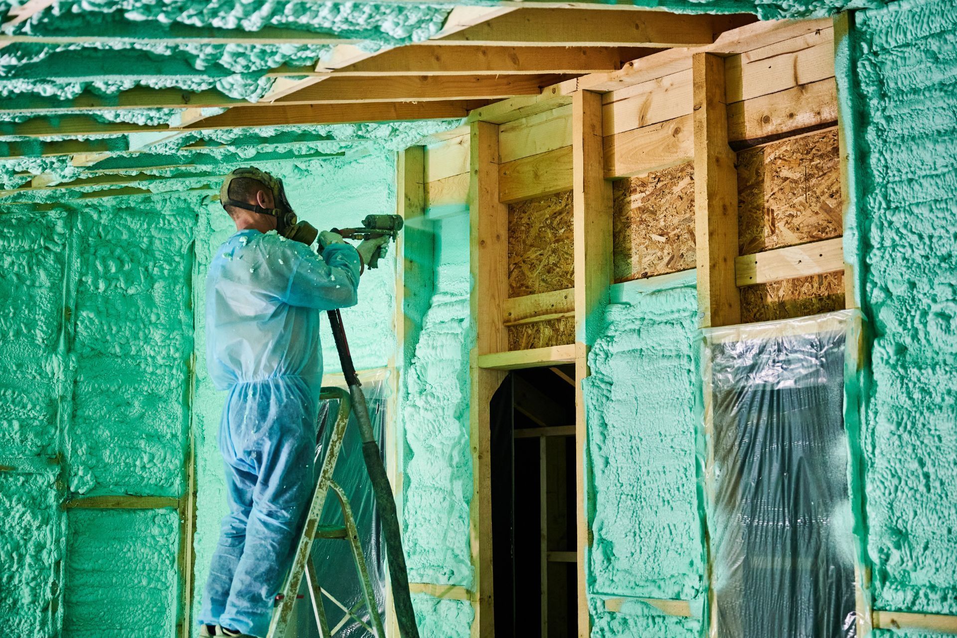 Worker spraying green foam insulation inside a wooden framed building
