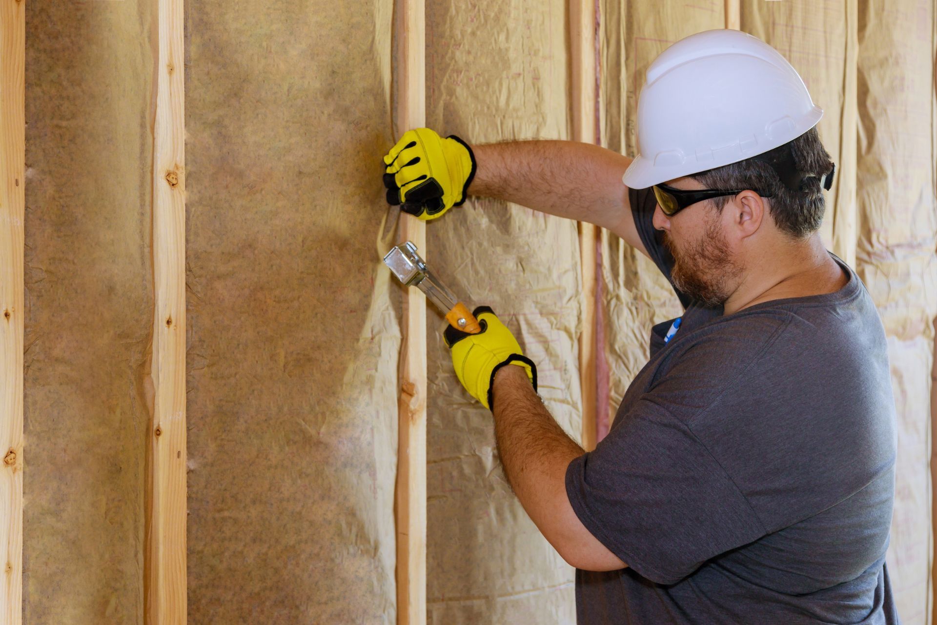 Worker in a white hard hat removing insulation from a wall with hand tools