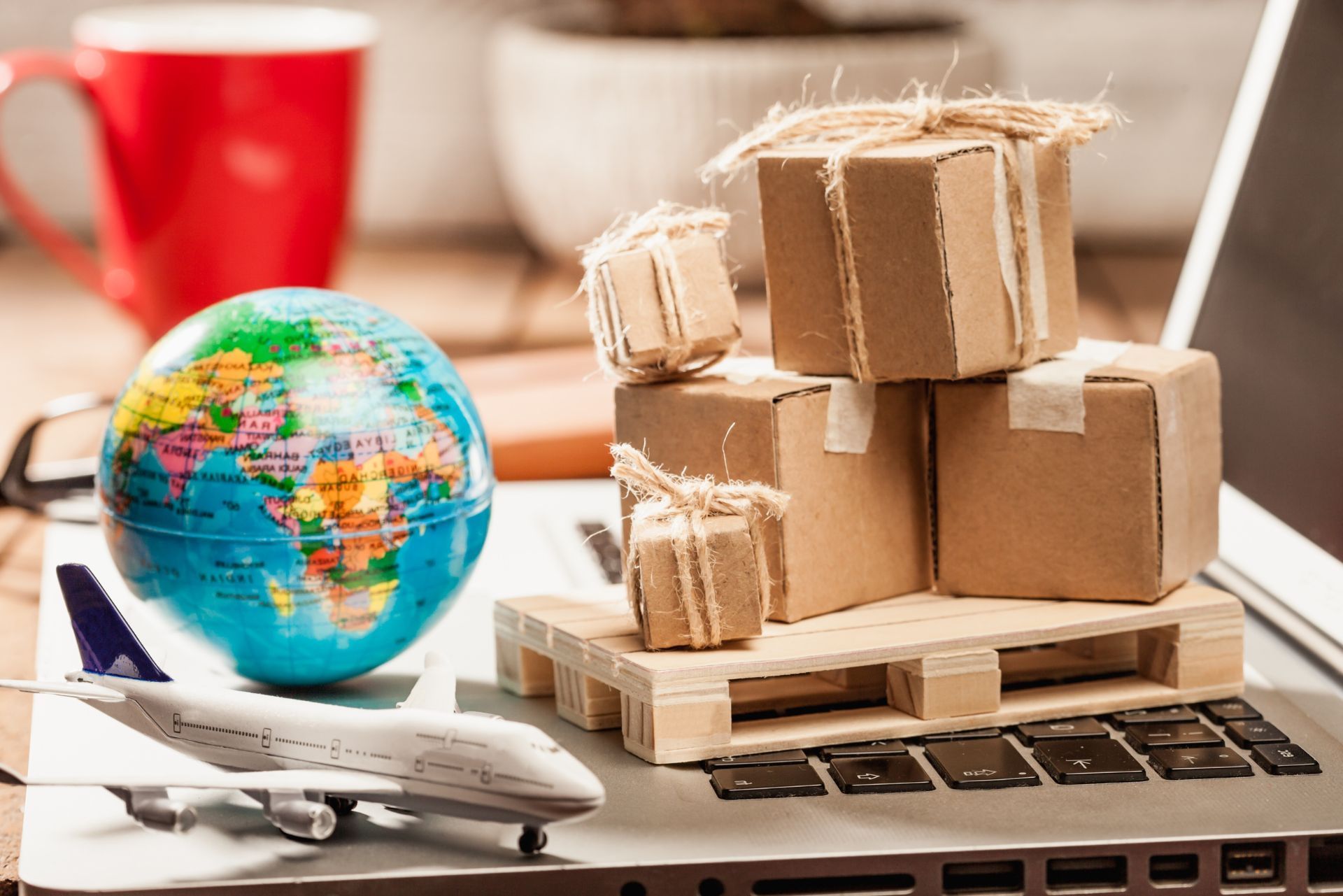 Mini globe, toy airplane, and cardboard boxes on a laptop, with a red mug in the background.