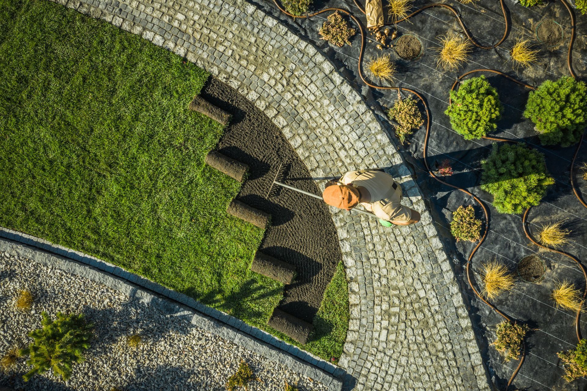 Overhead view of a person walking a cobblestone path beside a green lawn and landscaped rocks.
