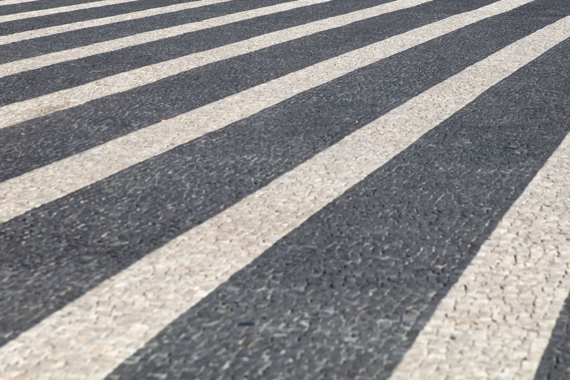 A close-up of a pedestrian crosswalk with alternating diagonal white and dark gray textured stripes.