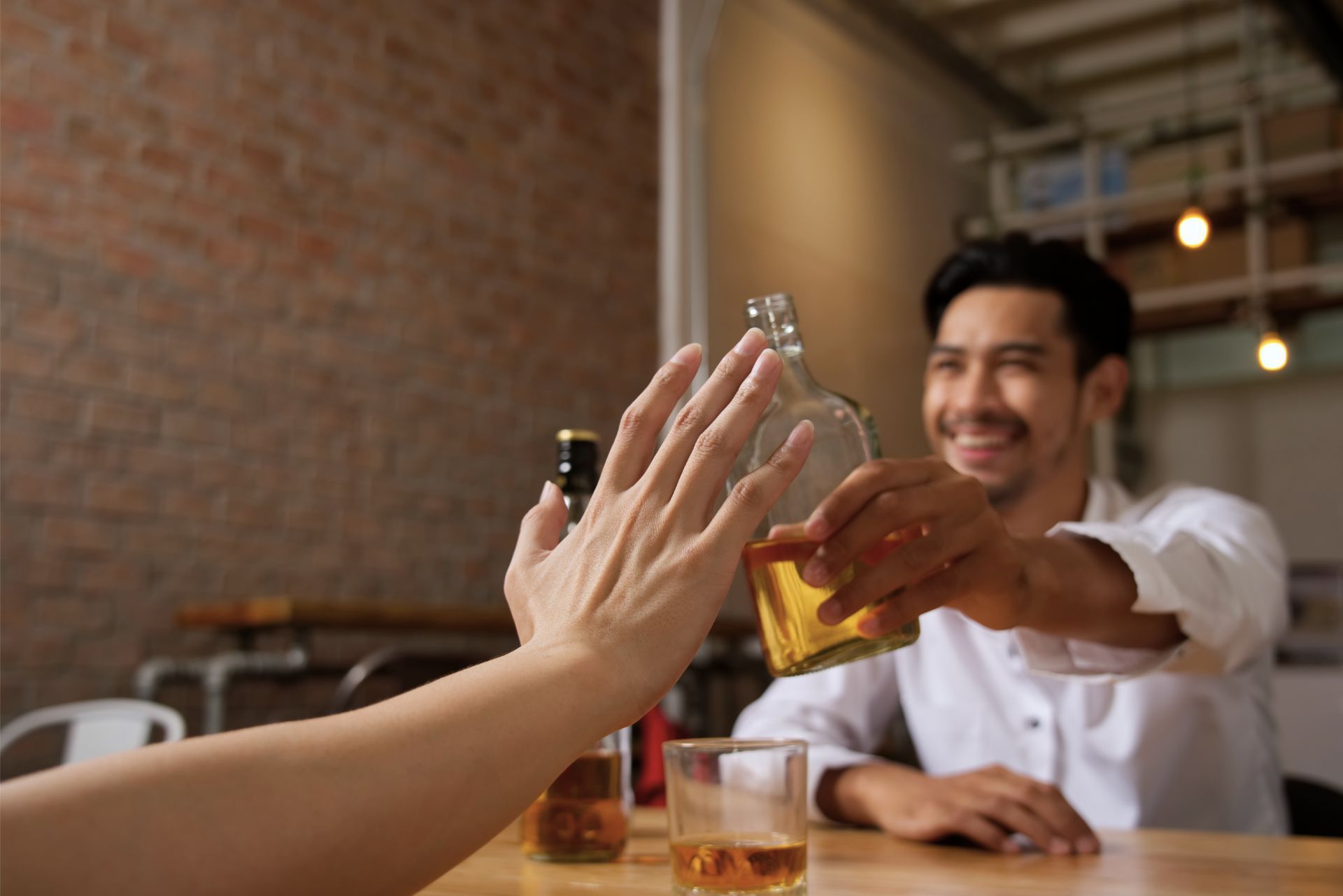 Friends clink whiskey glasses at a bar, smiling across a wooden table.
