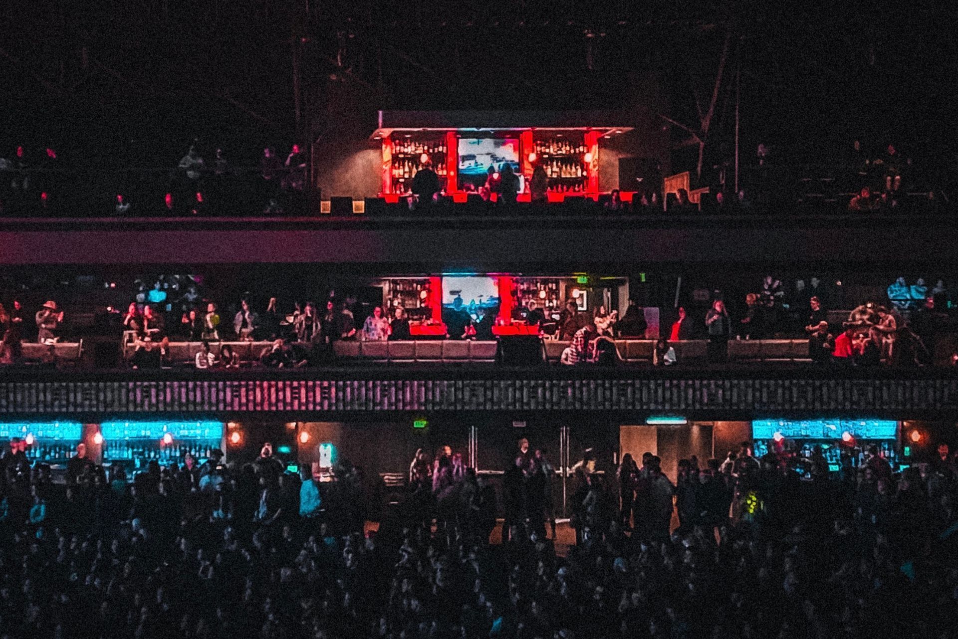 Crowded concert venue with red and blue stage lights and a large screen above the audience