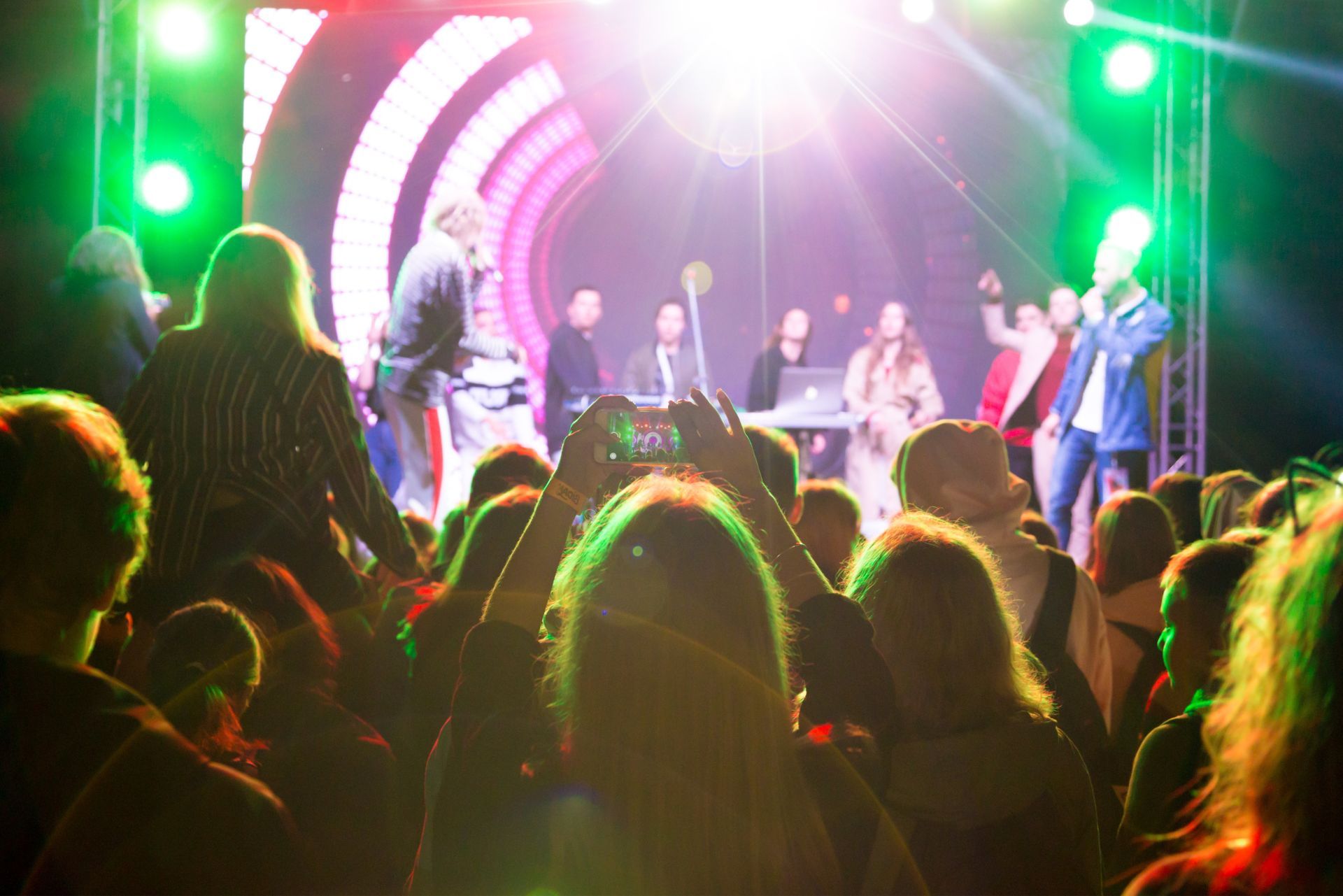 Crowd watching a brightly lit concert stage with green and pink lights