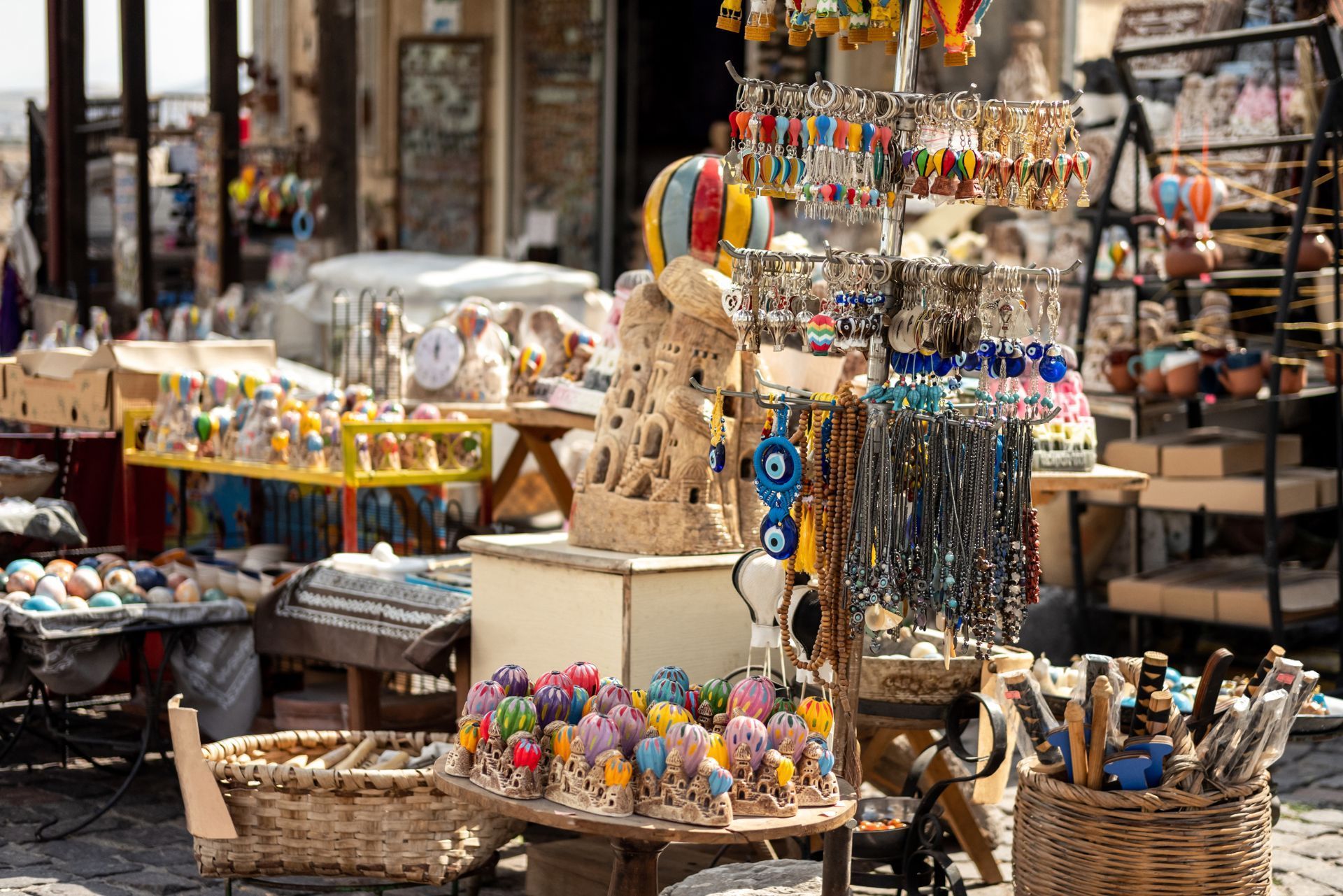 Street market stall filled with colorful handmade trinkets, jewelry, and baskets displayed outdoors