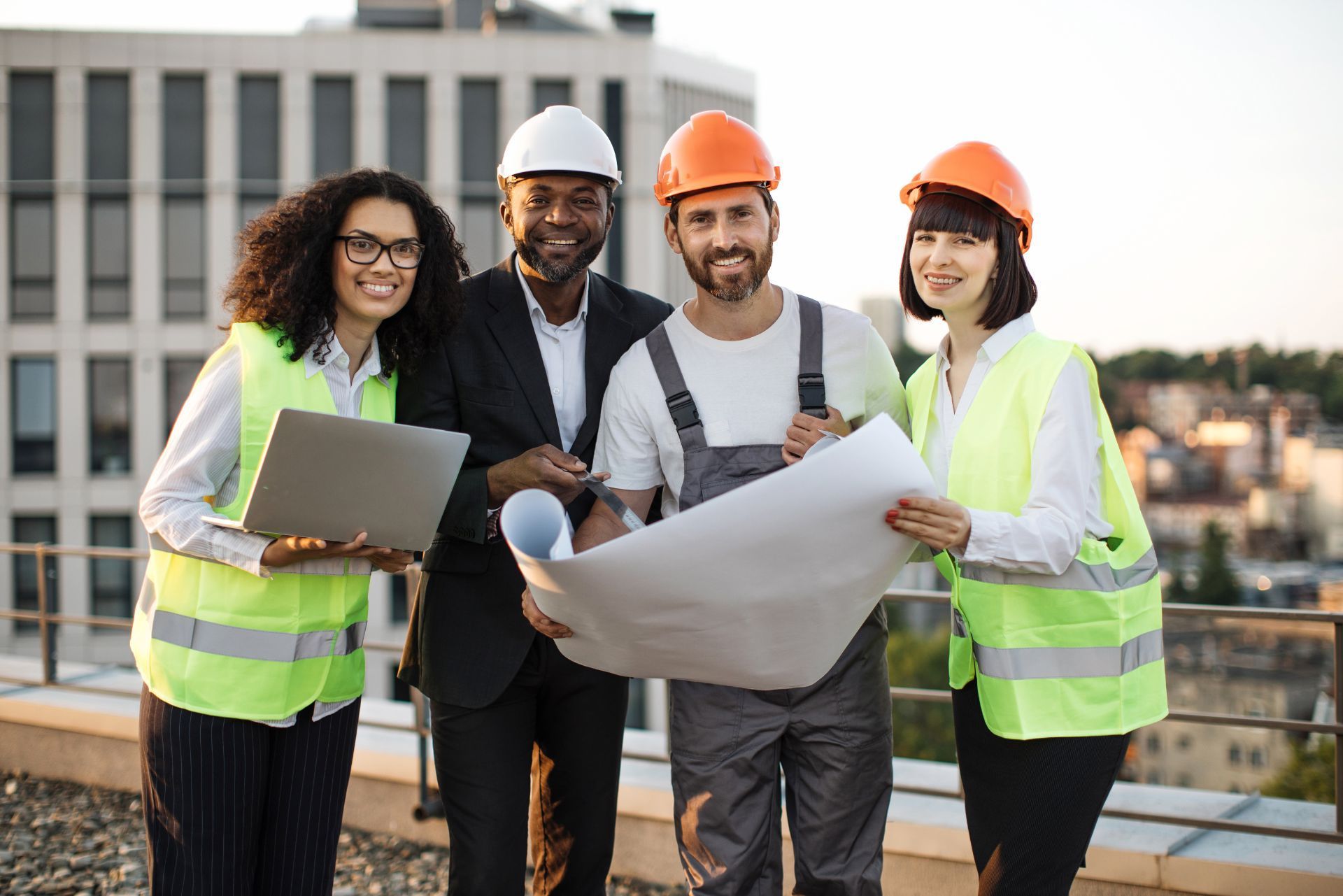 Four construction team members in safety vests and hard hats review blueprints at a rooftop site.