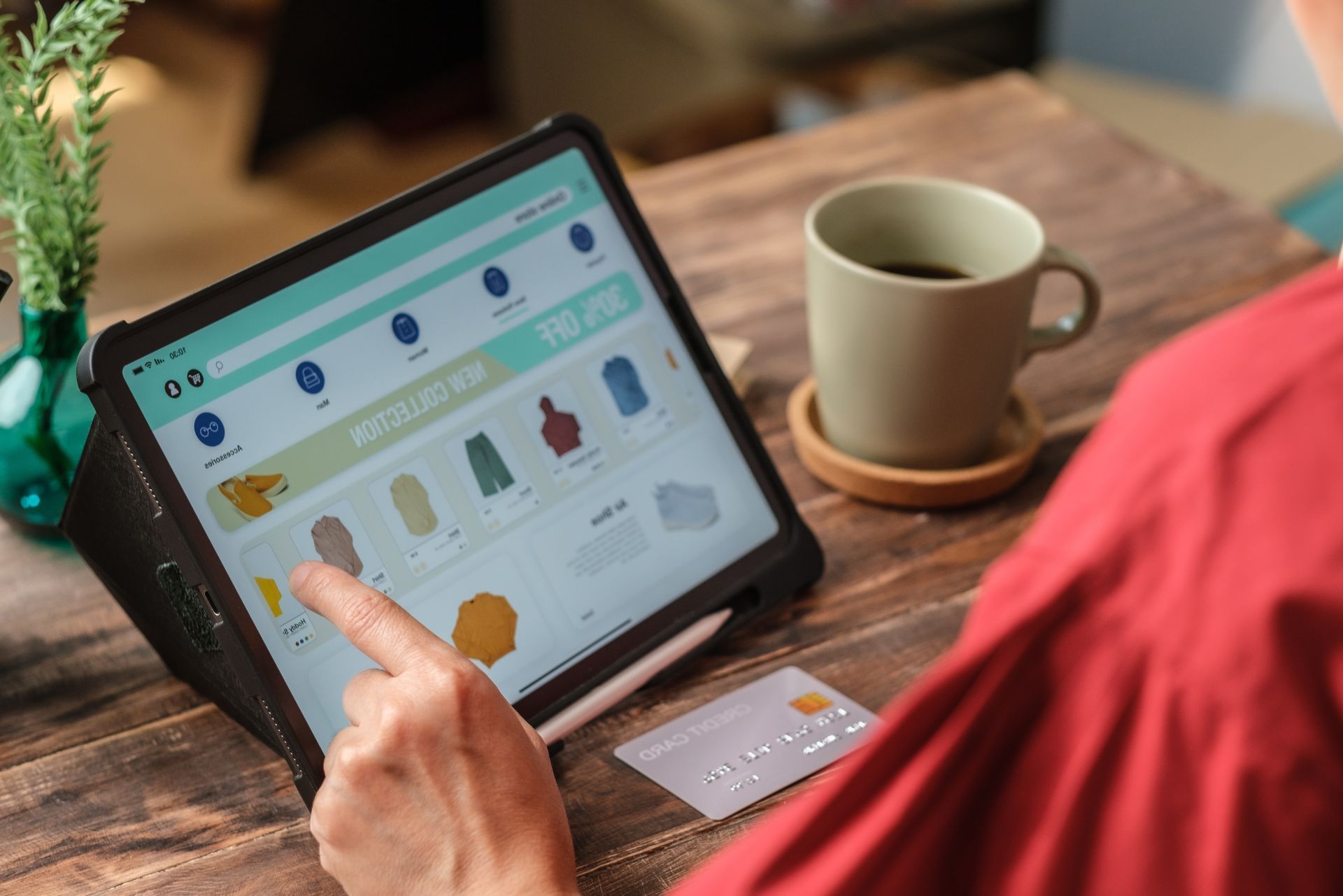 Person using a tablet with online shopping items beside a coffee mug on a wooden table
