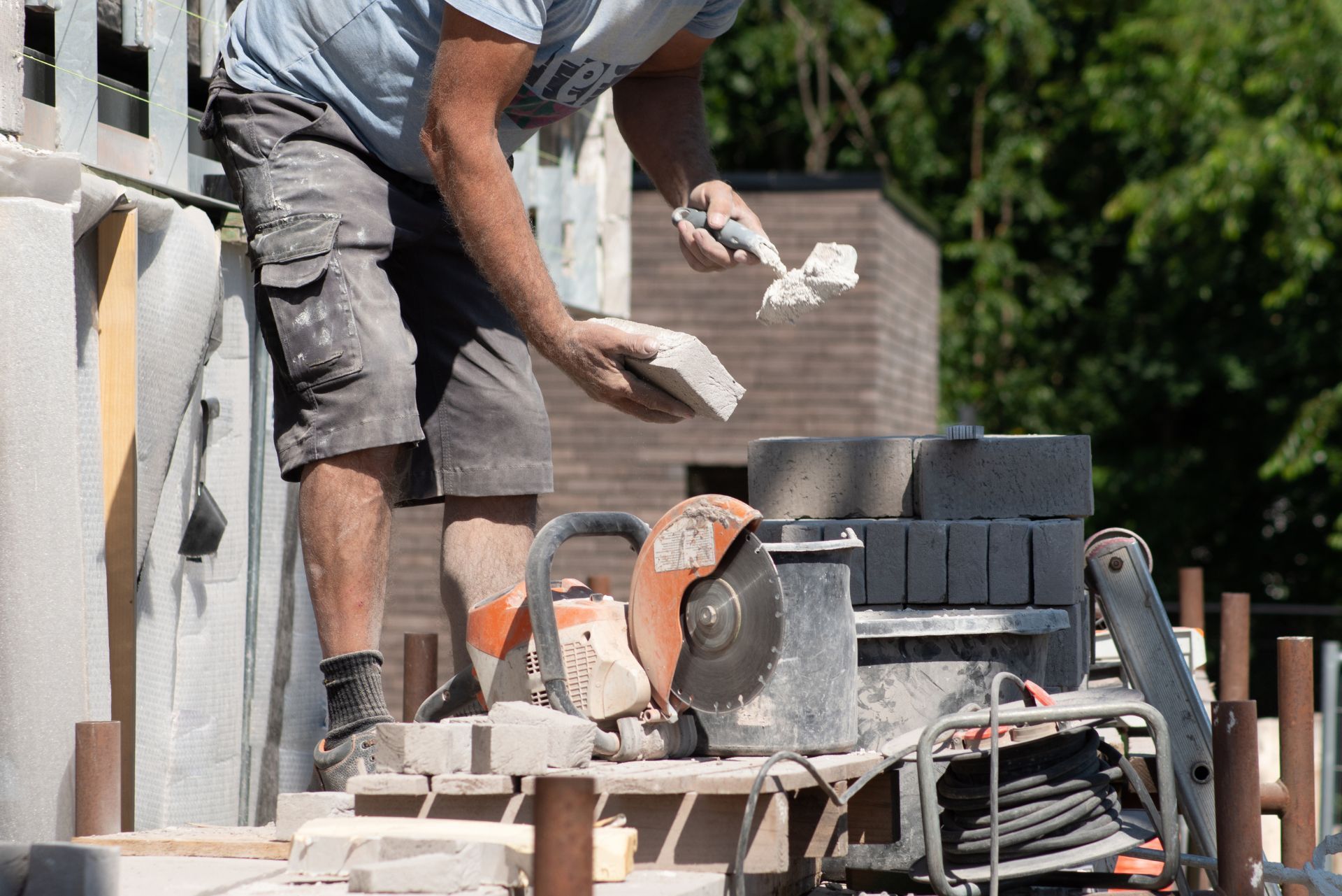Worker laying bricks beside a saw and stacked blocks at an outdoor construction site