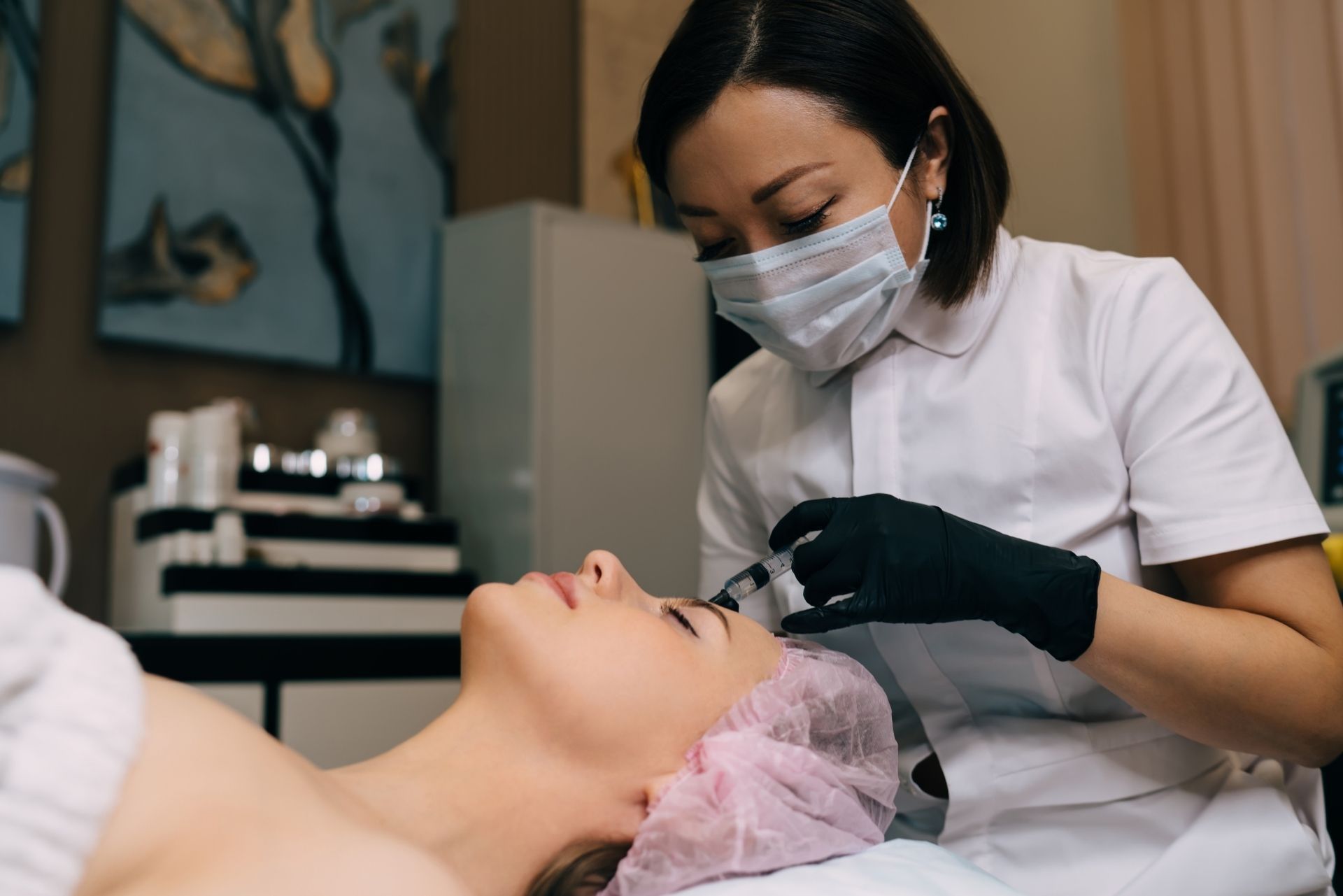 A professional in scrubs and a mask injects a cosmetic treatment into a patient's forehead at a clinic.