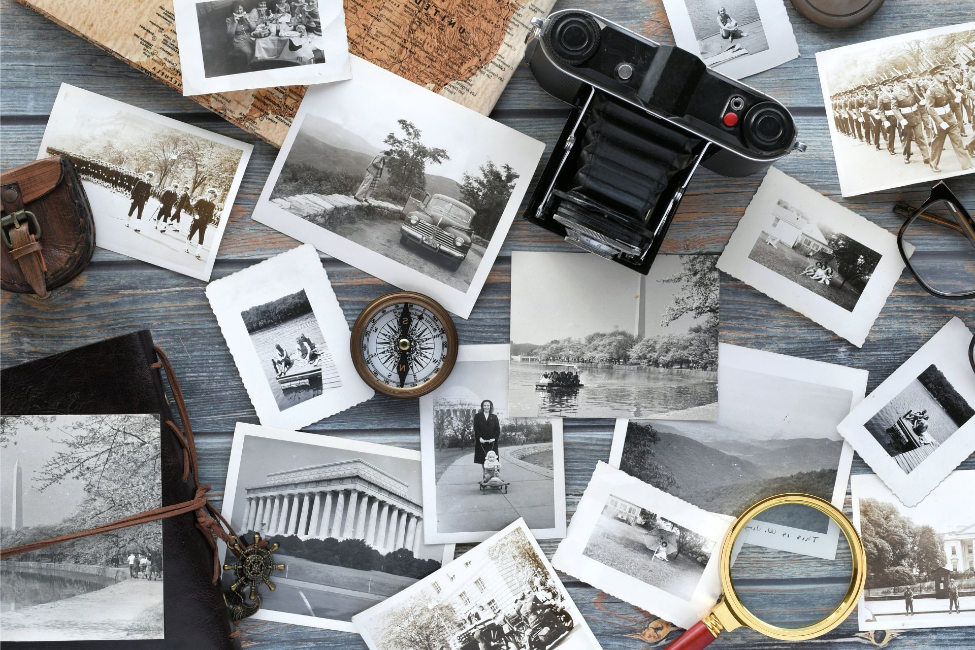Black-and-white photos scattered around a vintage camera and magnifying glass on a wooden surface