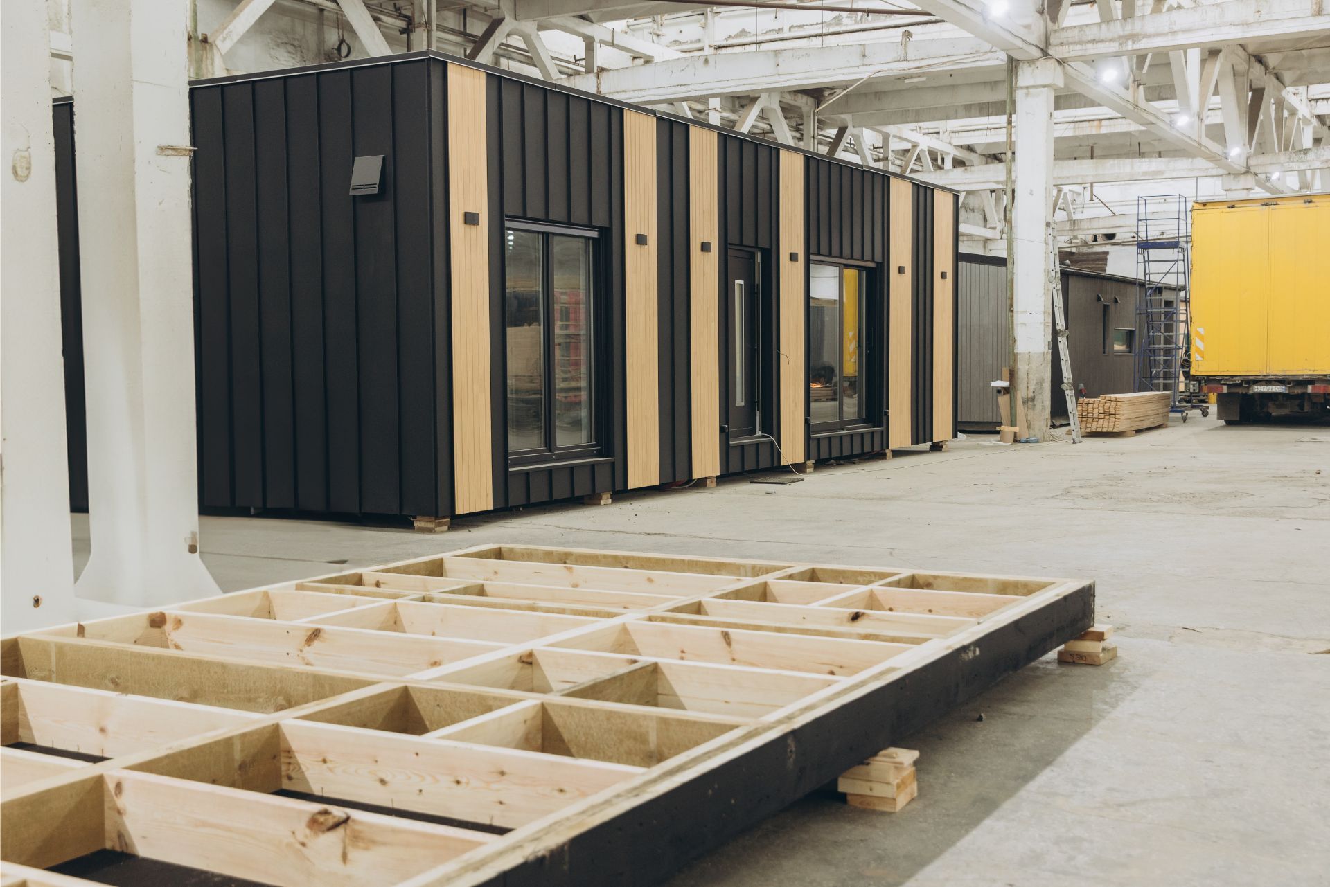 Industrial warehouse with modular black-and-tan room units and wooden frames on the floor