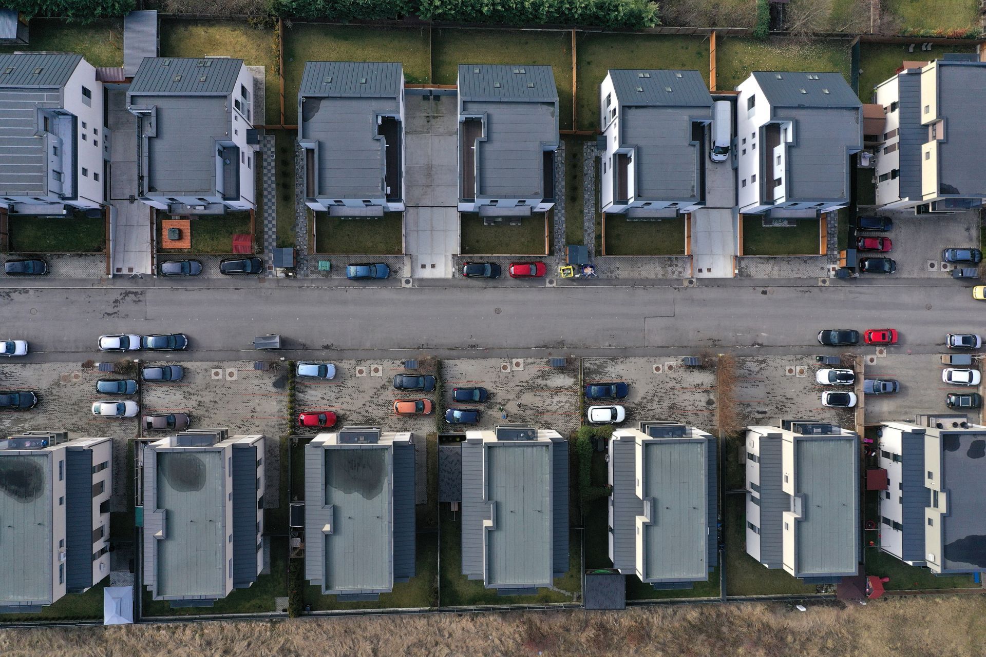 Aerial view of two rows of modern, flat-roofed houses separated by a street with parked cars.