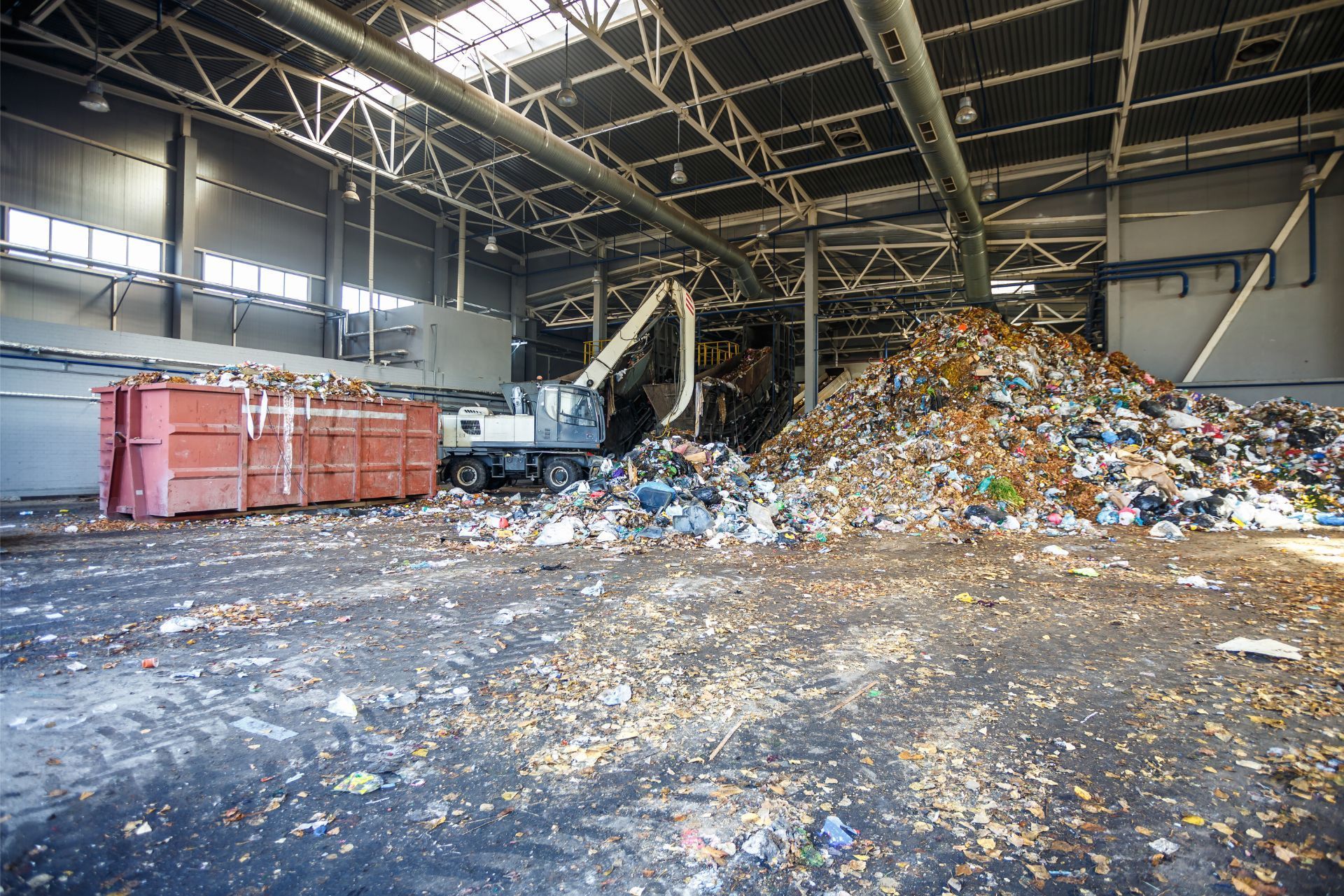 Indoor recycling facility with piles of sorted waste and a large metal loader near red bins