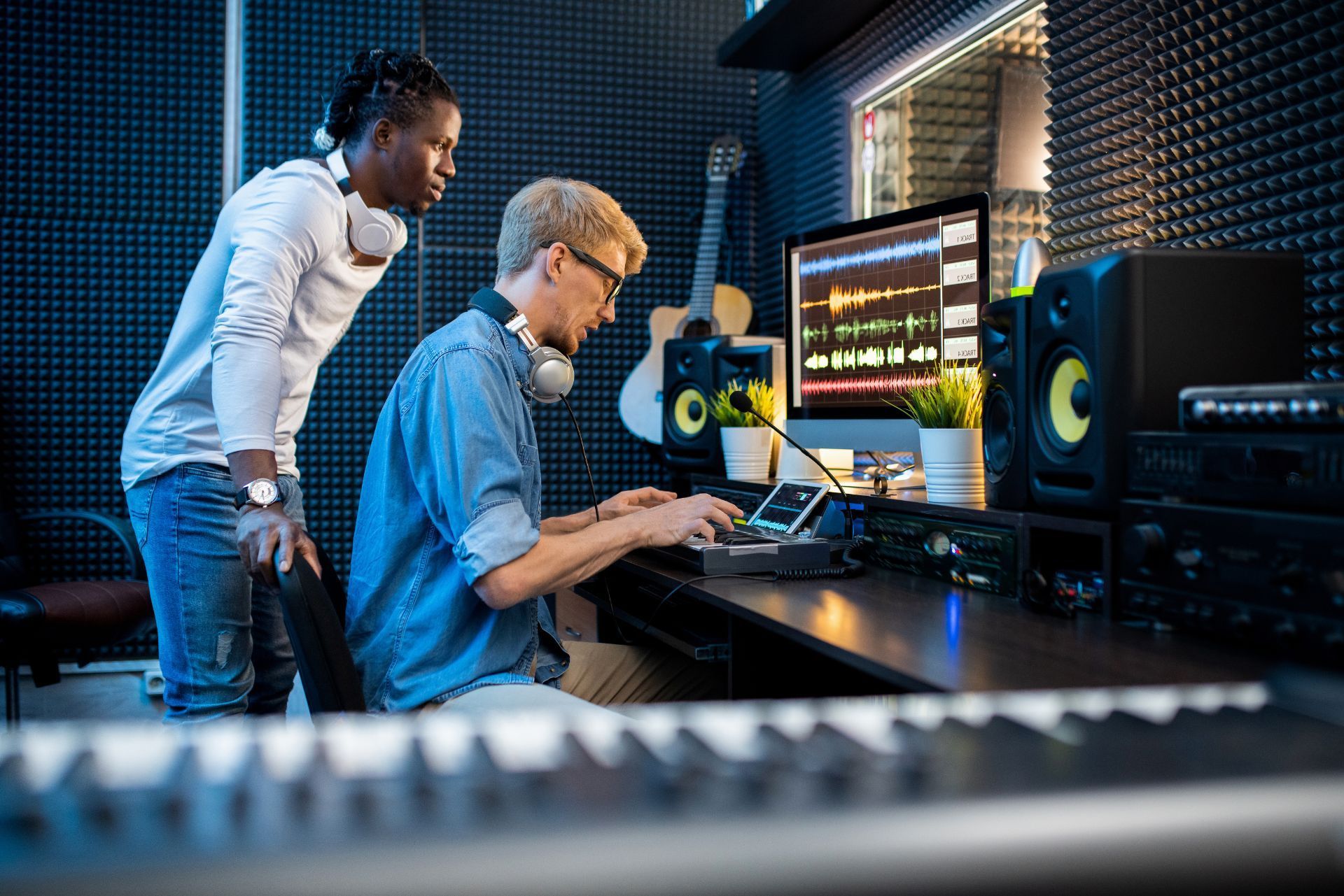 Two people working in a sound studio, editing audio on a computer with monitors and speakers nearby.