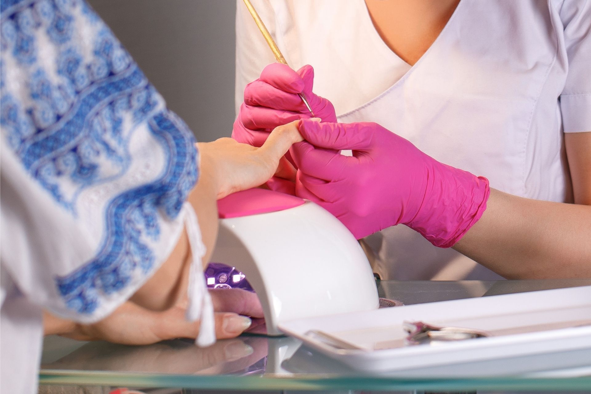 Gloved hands giving a manicure, filing a client’s fingernails at a salon table