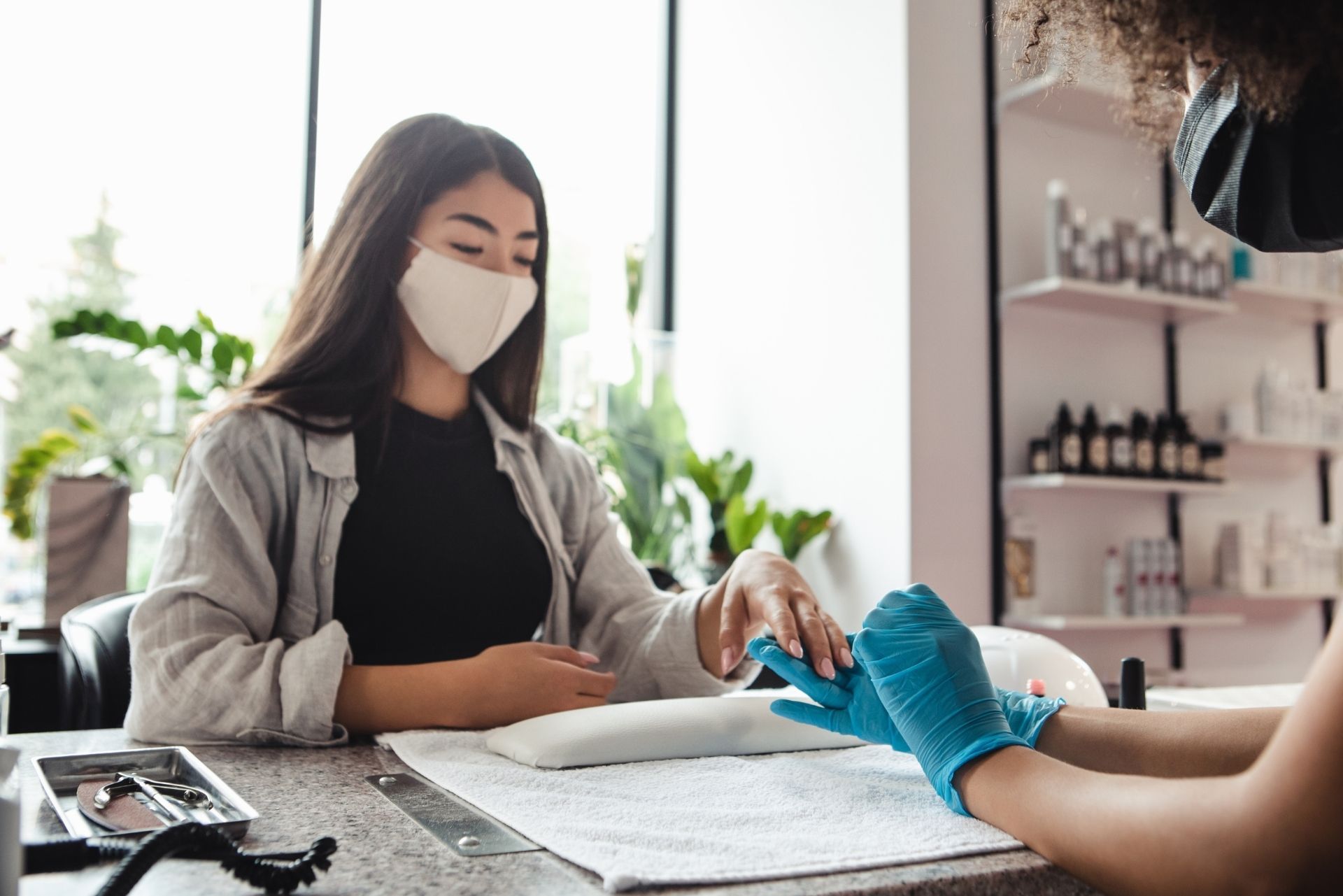 Client receiving a manicure at a nail salon, with a masked technician working on her nails.