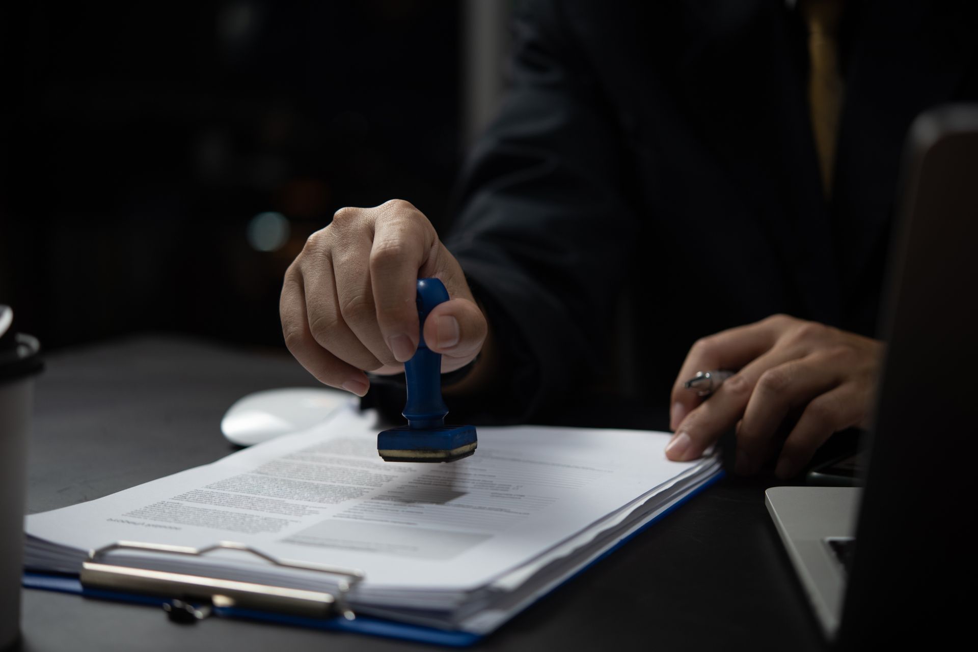 Hand stamping a document on a desk beside a laptop and white mouse