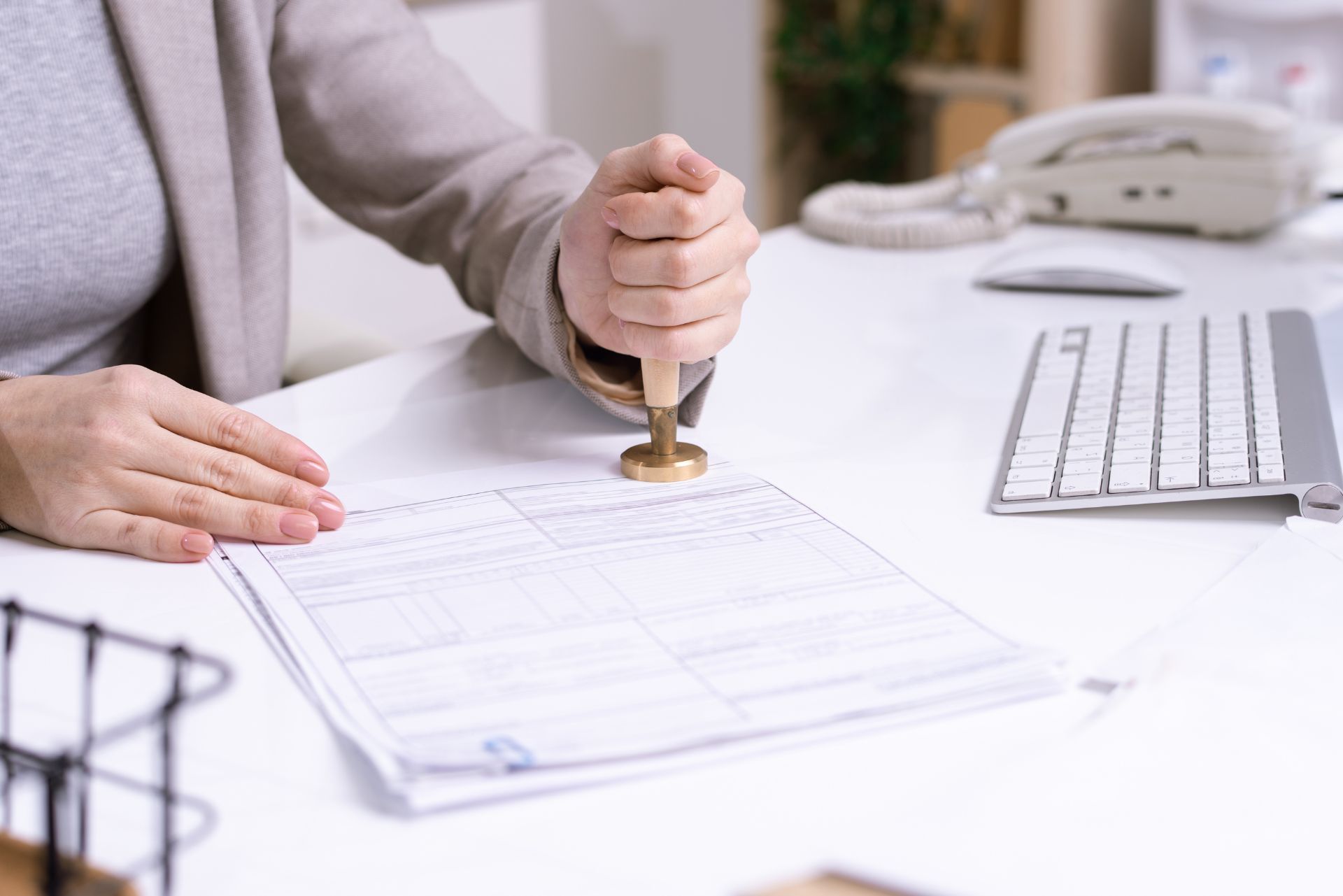 Hand stamping a document on a white desk beside a keyboard and telephone