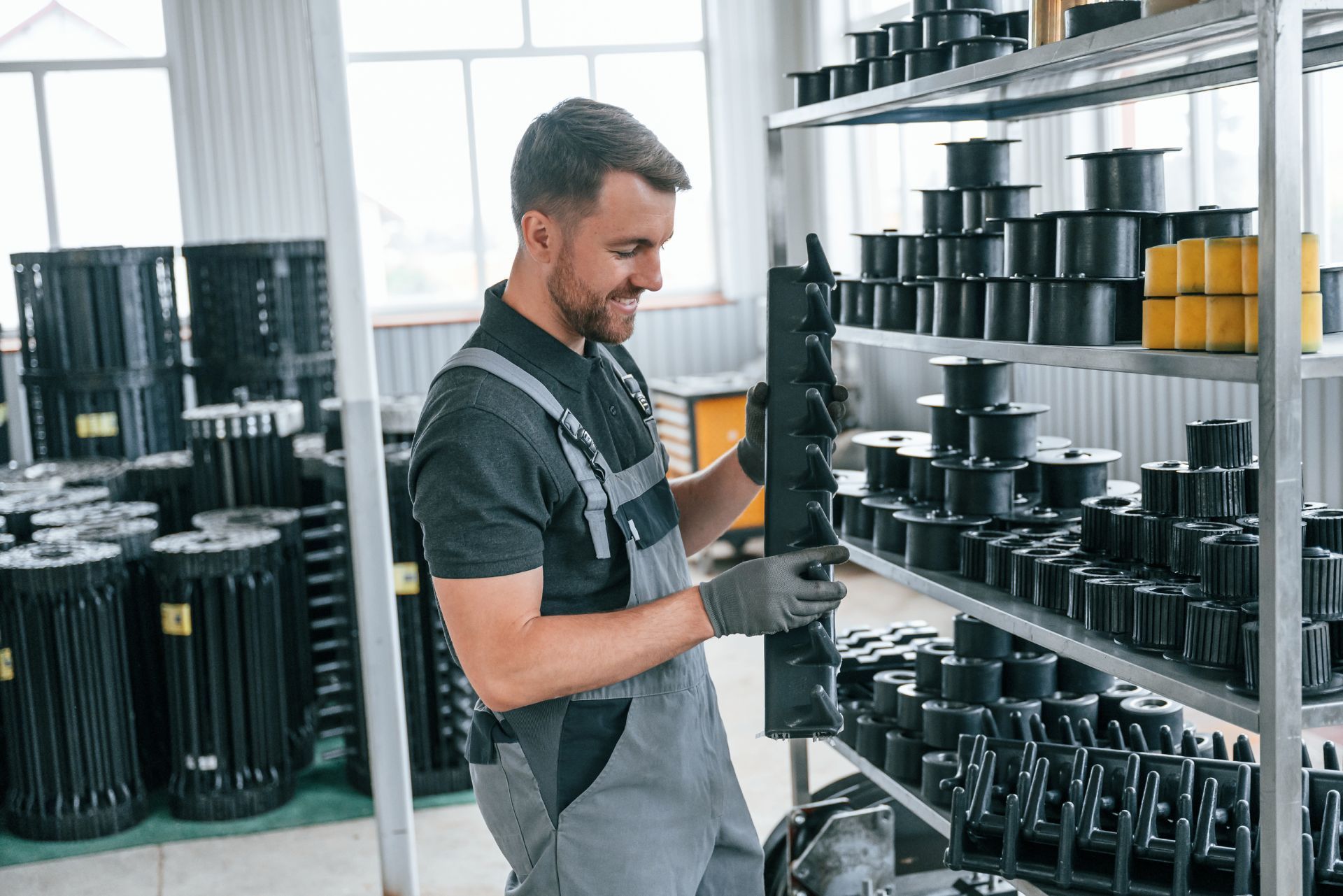 Worker in gray apron organizing black containers on metal shelves in a bright warehouse