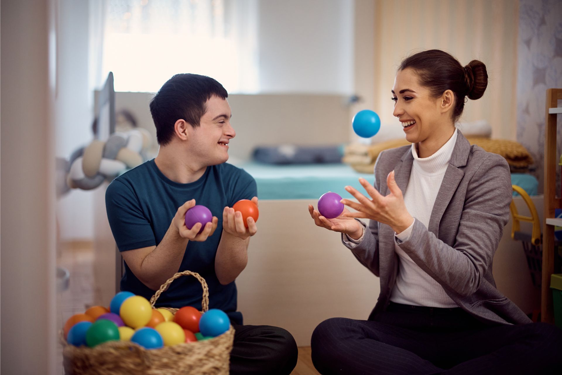 Two people smiling and tossing colorful balls during a playful indoor activity session