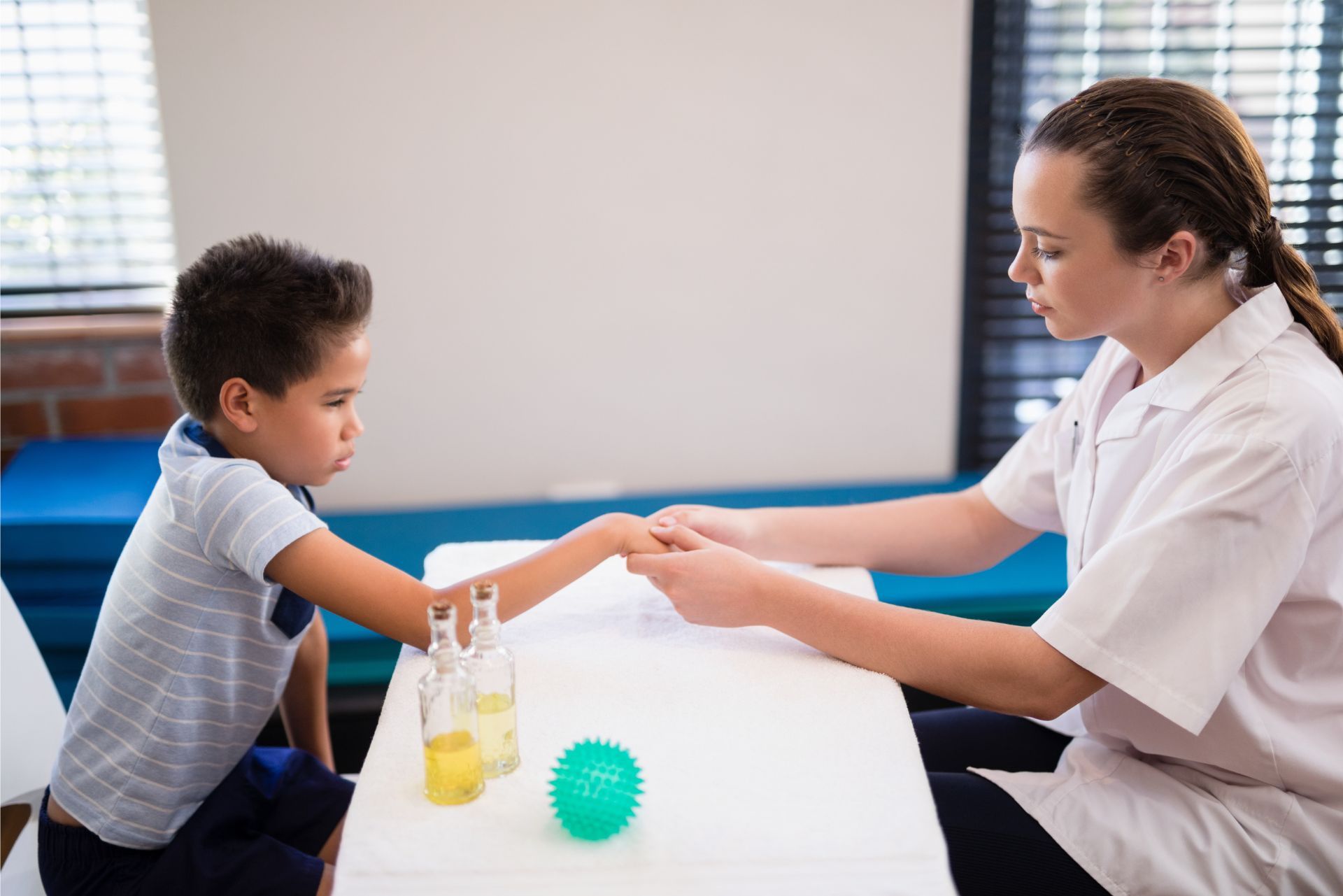 Therapist and child reaching hands across a table with toys in a bright therapy room