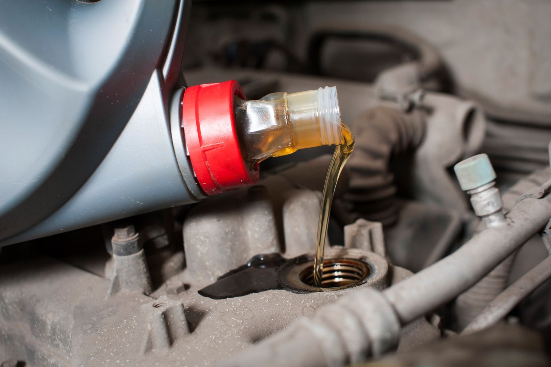 Oil pouring from a red funnel into an engine fill opening in a car engine bay