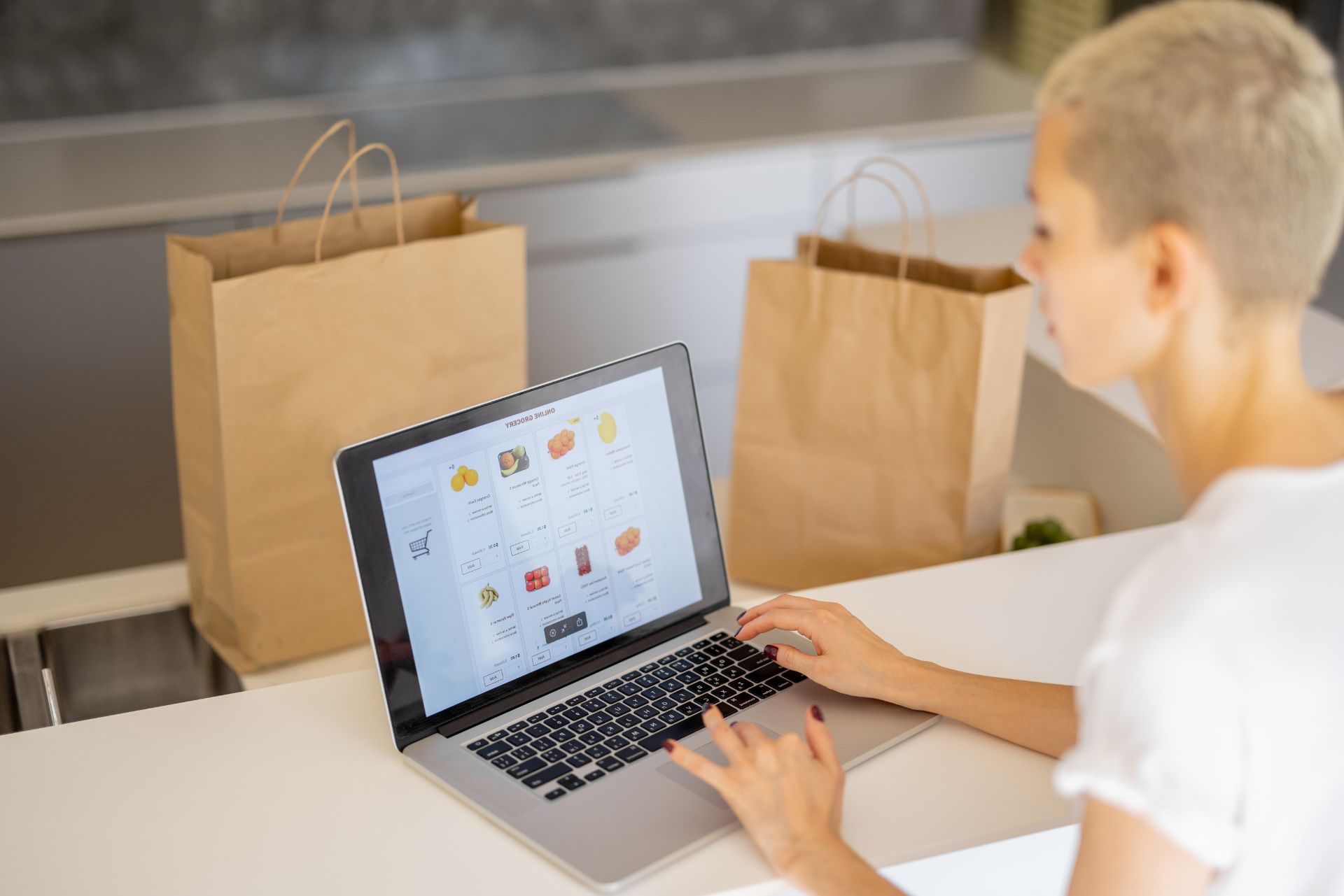Person using a laptop beside shopping bags in a bright kitchen