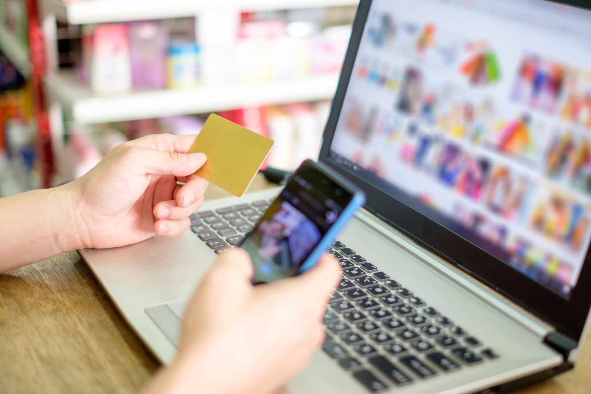 Hands holding a credit card and phone over a laptop for online shopping