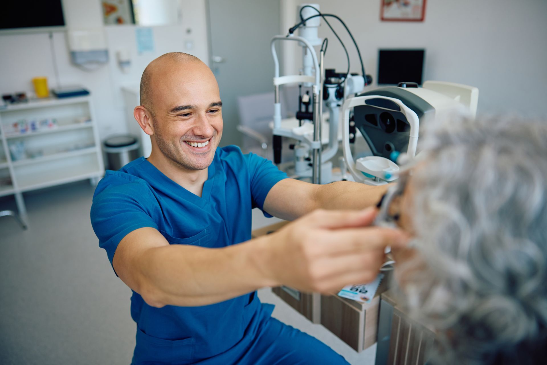 Eye doctor examining a smiling patient in a clinic with medical equipment nearby