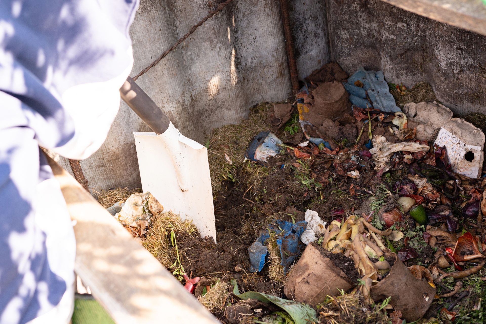 Overhead view of a trash-filled concrete pit with debris, food scraps, and a person’s sleeve at the edge