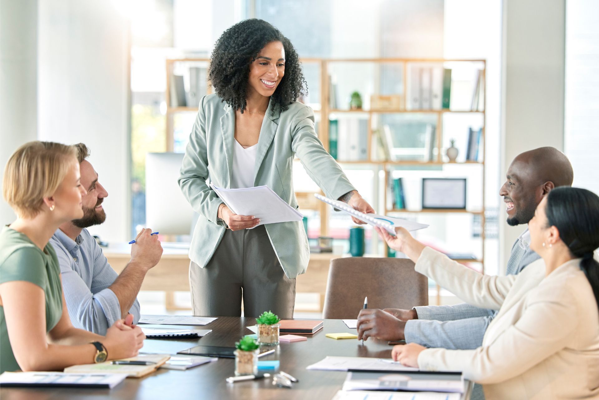 Team meeting in a bright office, with one woman presenting papers to coworkers around a conference table.