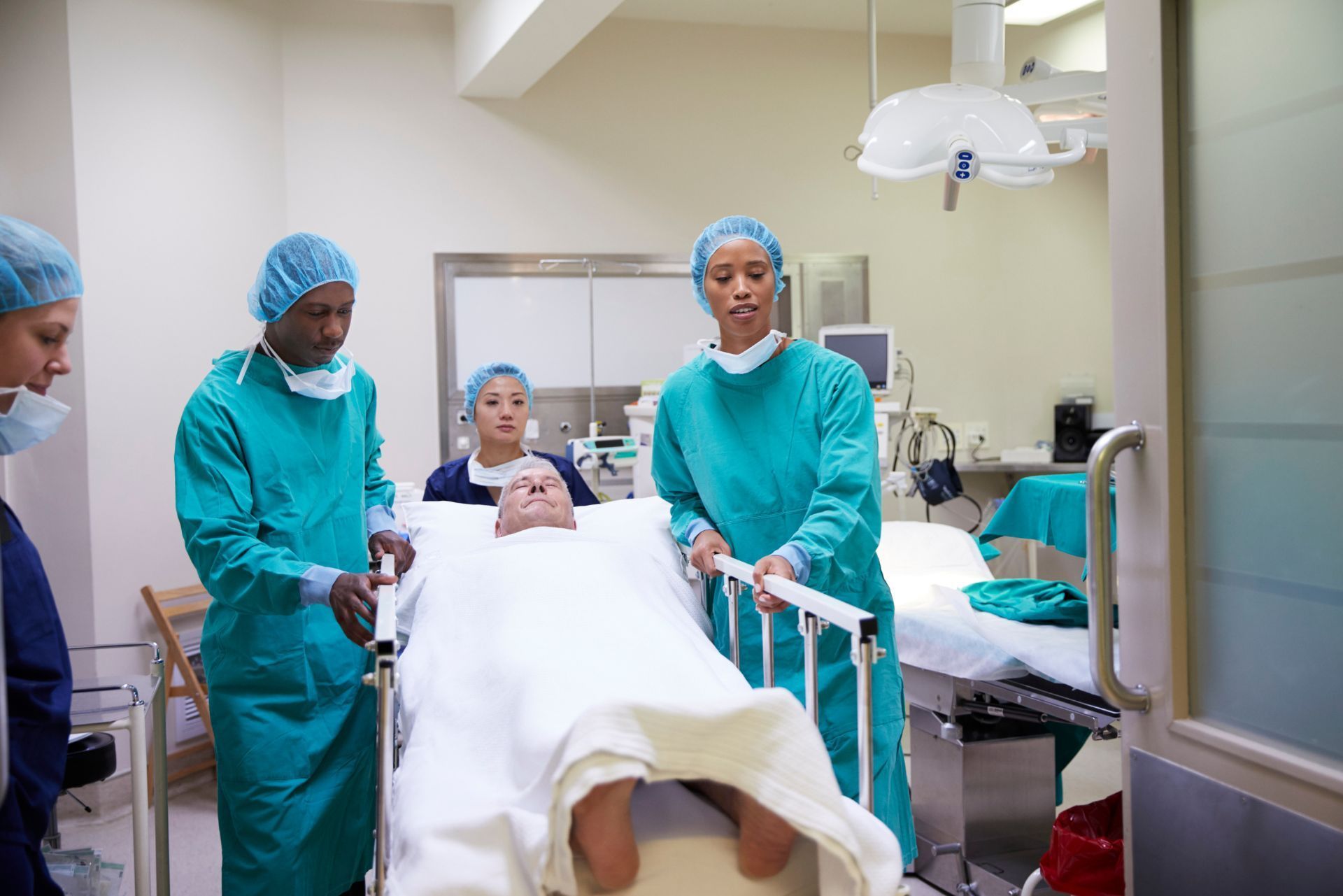 Hospital staff in teal scrubs and caps wheel a patient on a stretcher down a corridor.