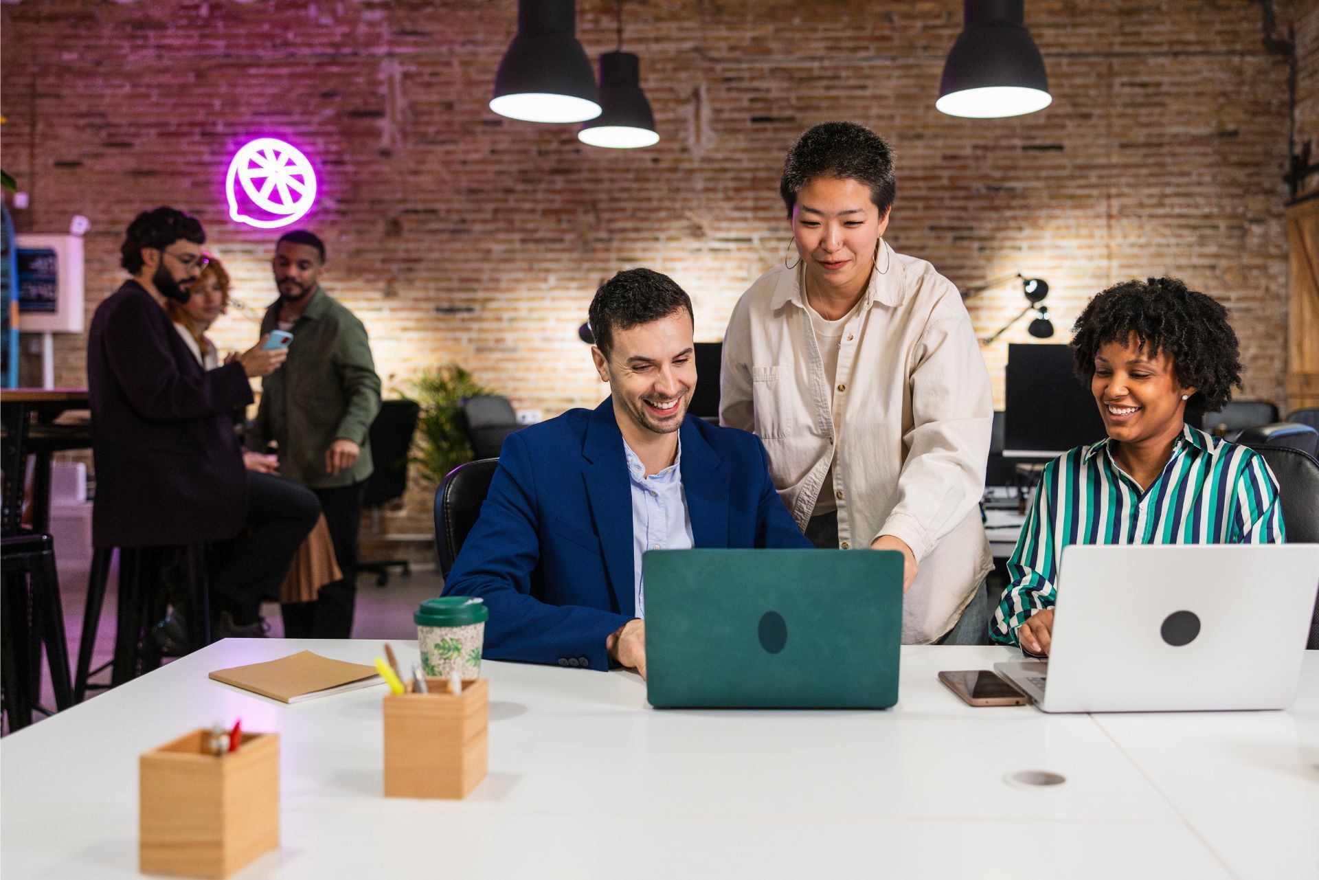 People collaborating at laptops in a brick-walled coworking space with warm hanging lights