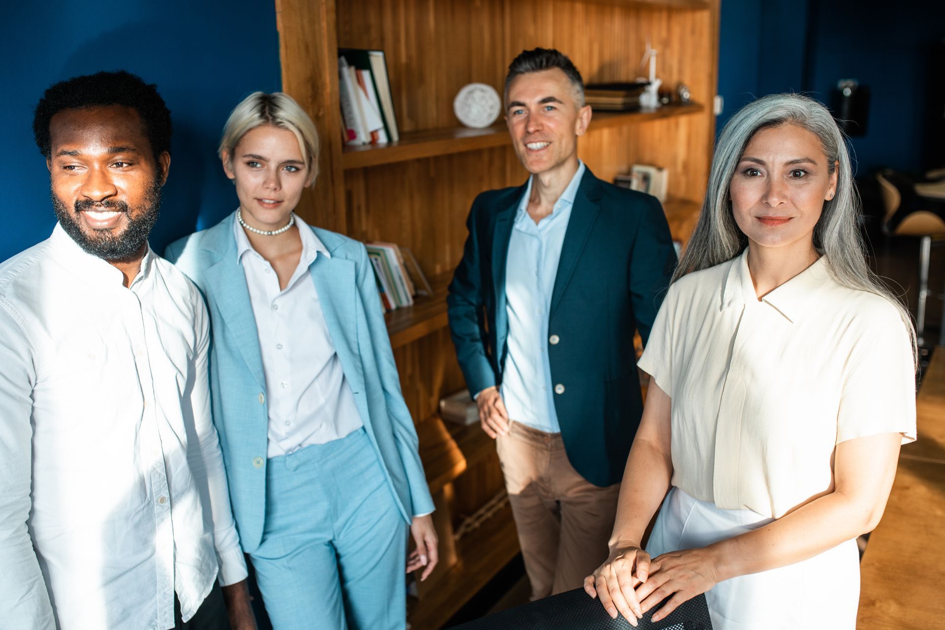 Four professionals standing in an office, with shelves and books in the background