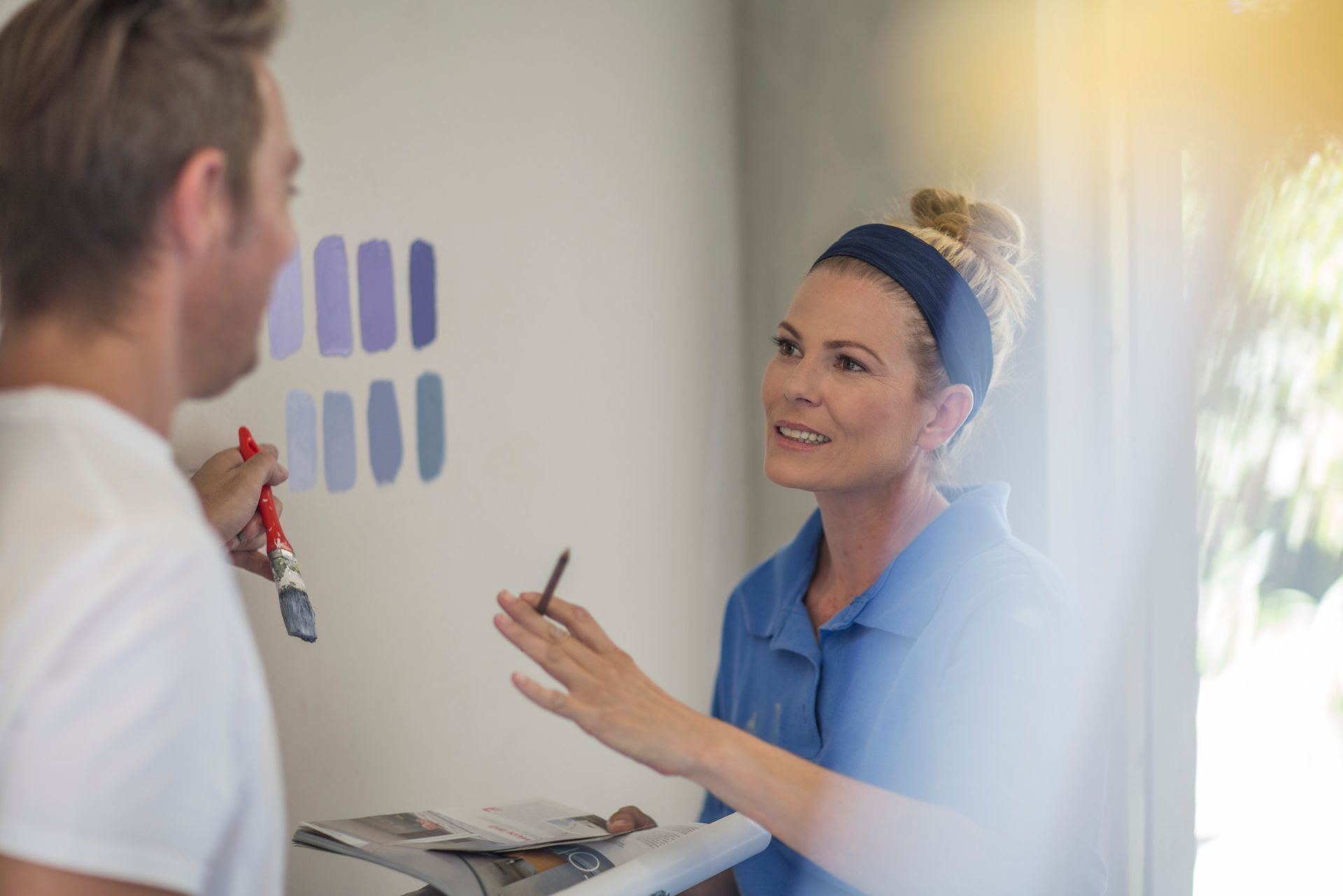 Woman in blue shirt speaking with man near wall paint swatches in a bright room