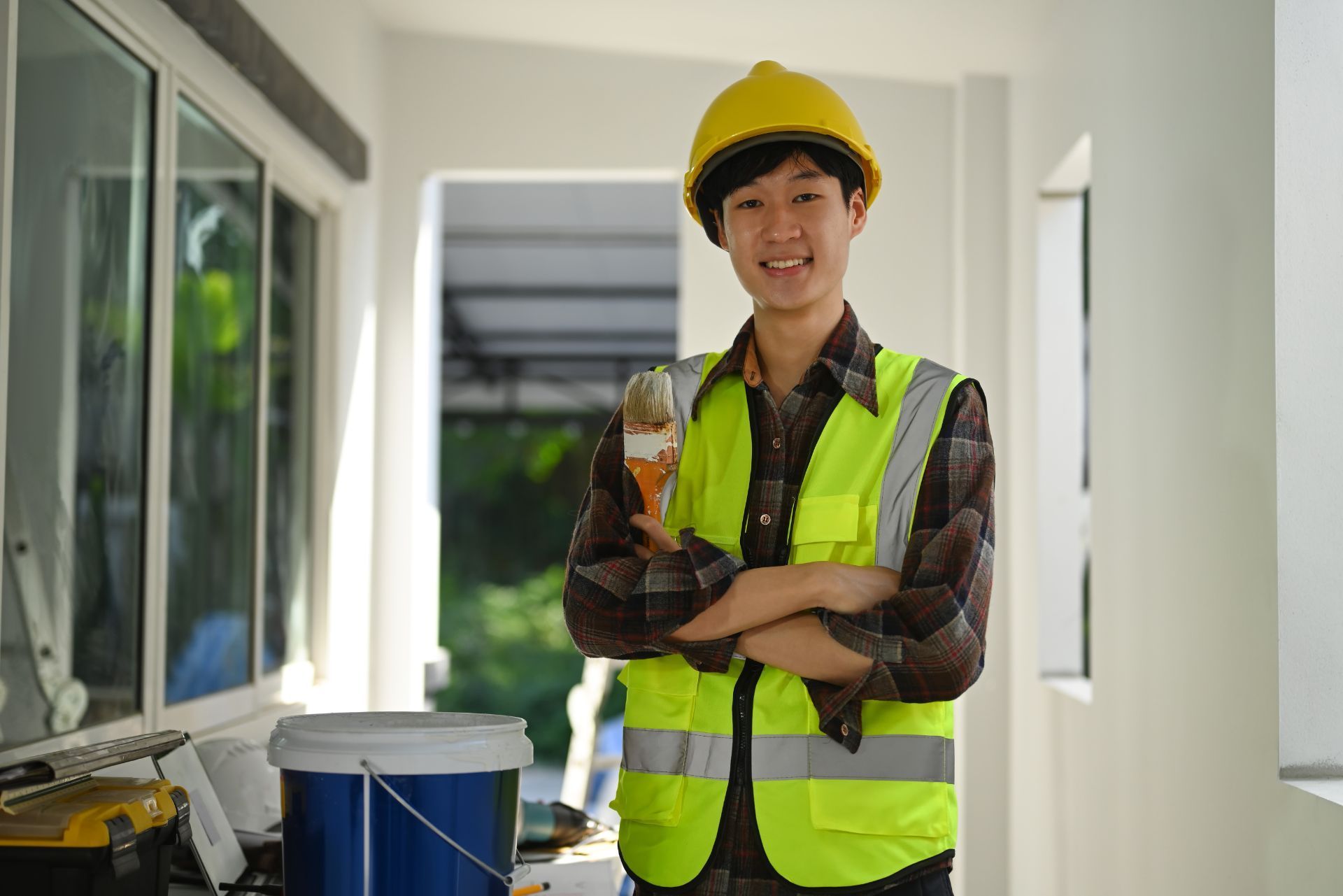 Construction worker in a yellow hard hat and safety vest holding a drink in a bright hallway